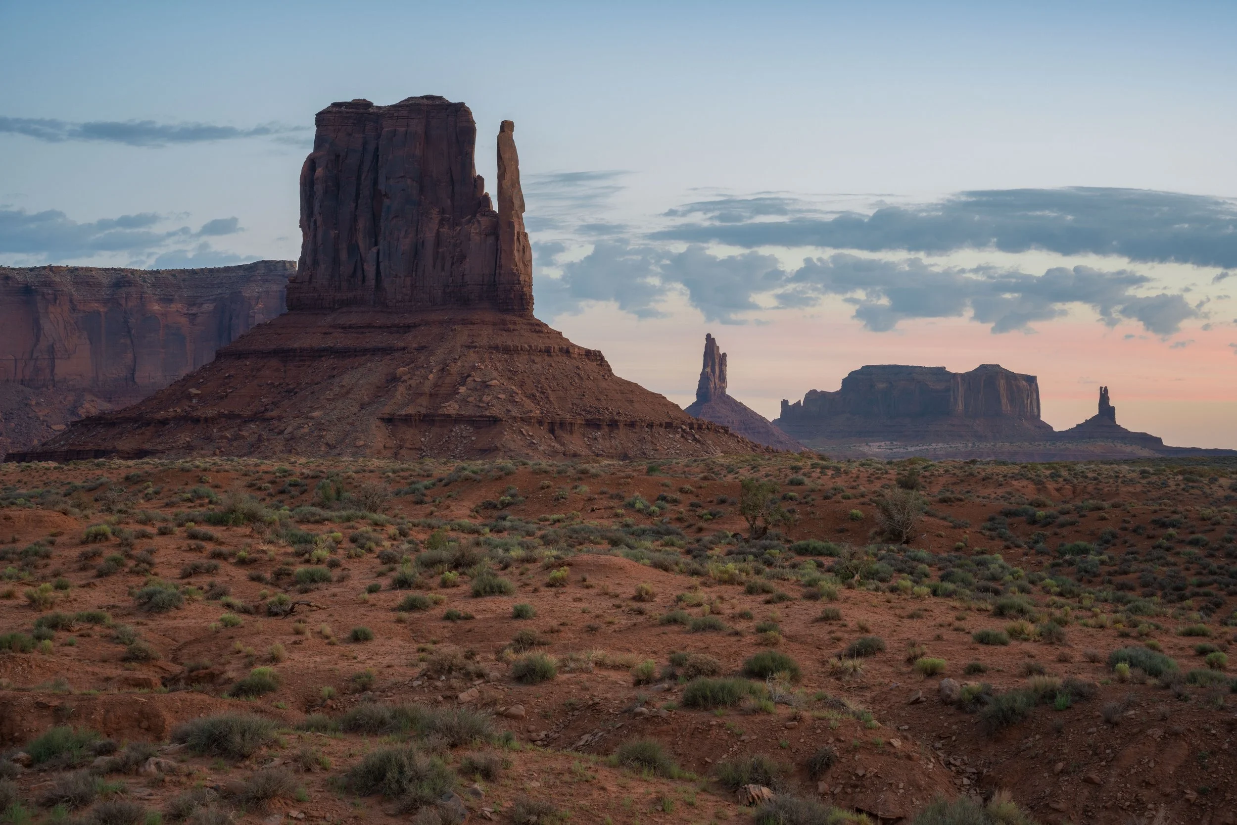 Monument Valley at sunrise, showing red sandstone formations, desert terrain, and soft golden light across the landscape