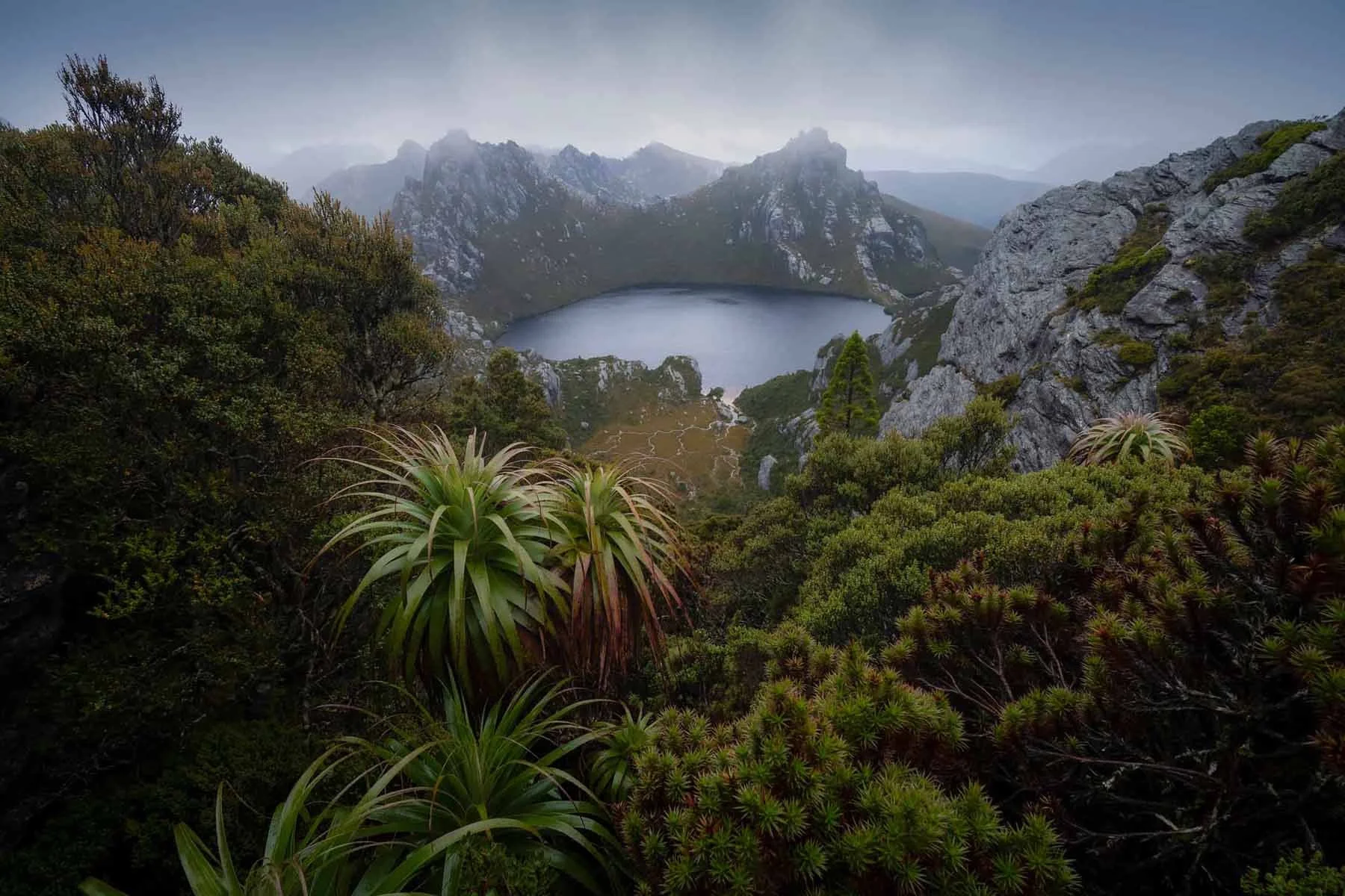 Clouds break and reveal a moody Lake Oberon in the Southwest National Park, Tasmania