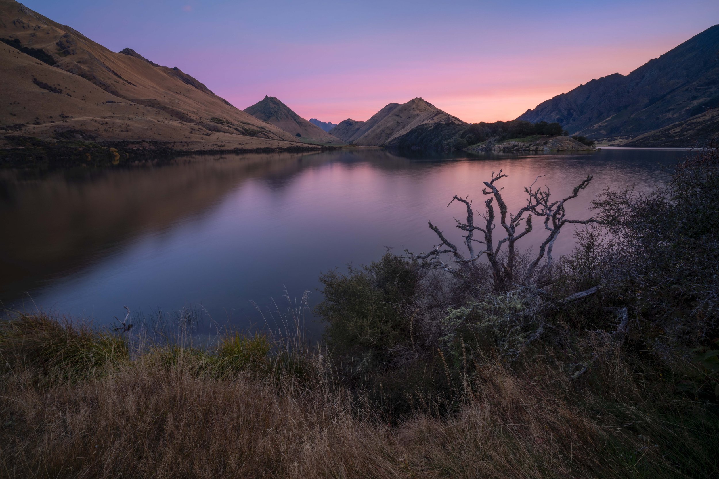Moke Lake near Queenstown, New Zealand, reflecting the surrounding mountains and golden tussock landscape beneath dramatic alpine skies.