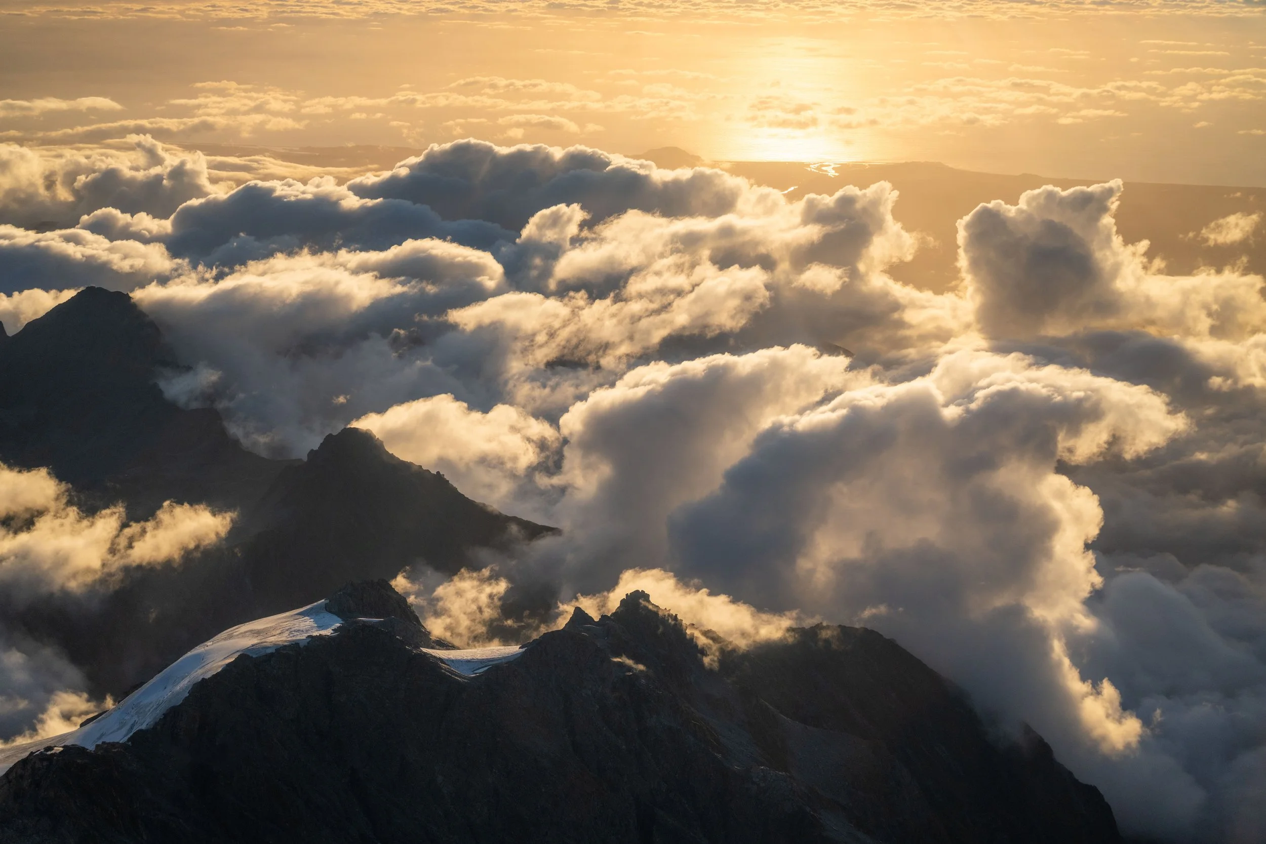 Sunset light illuminating rocky mountain peaks and clouds from above