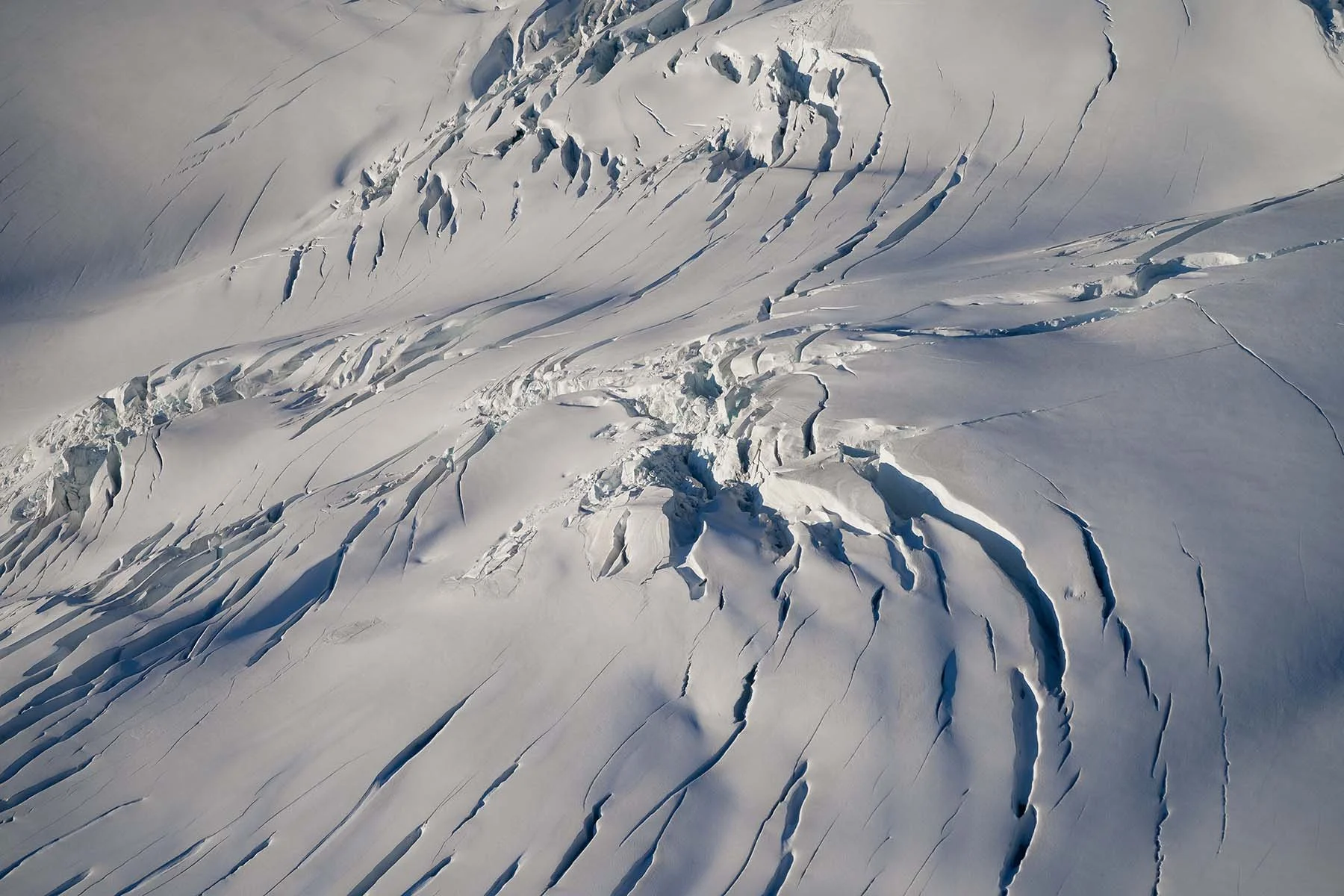 Aerial perspective of glacier crevasses with shadows highlighting depth