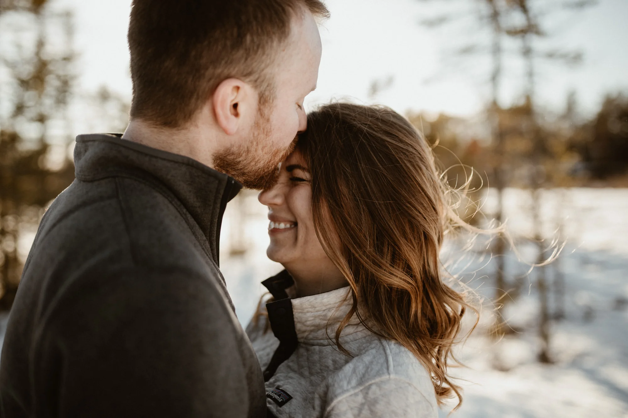 Guy kissing his fiancé on her forehead with the sun glowing behind them