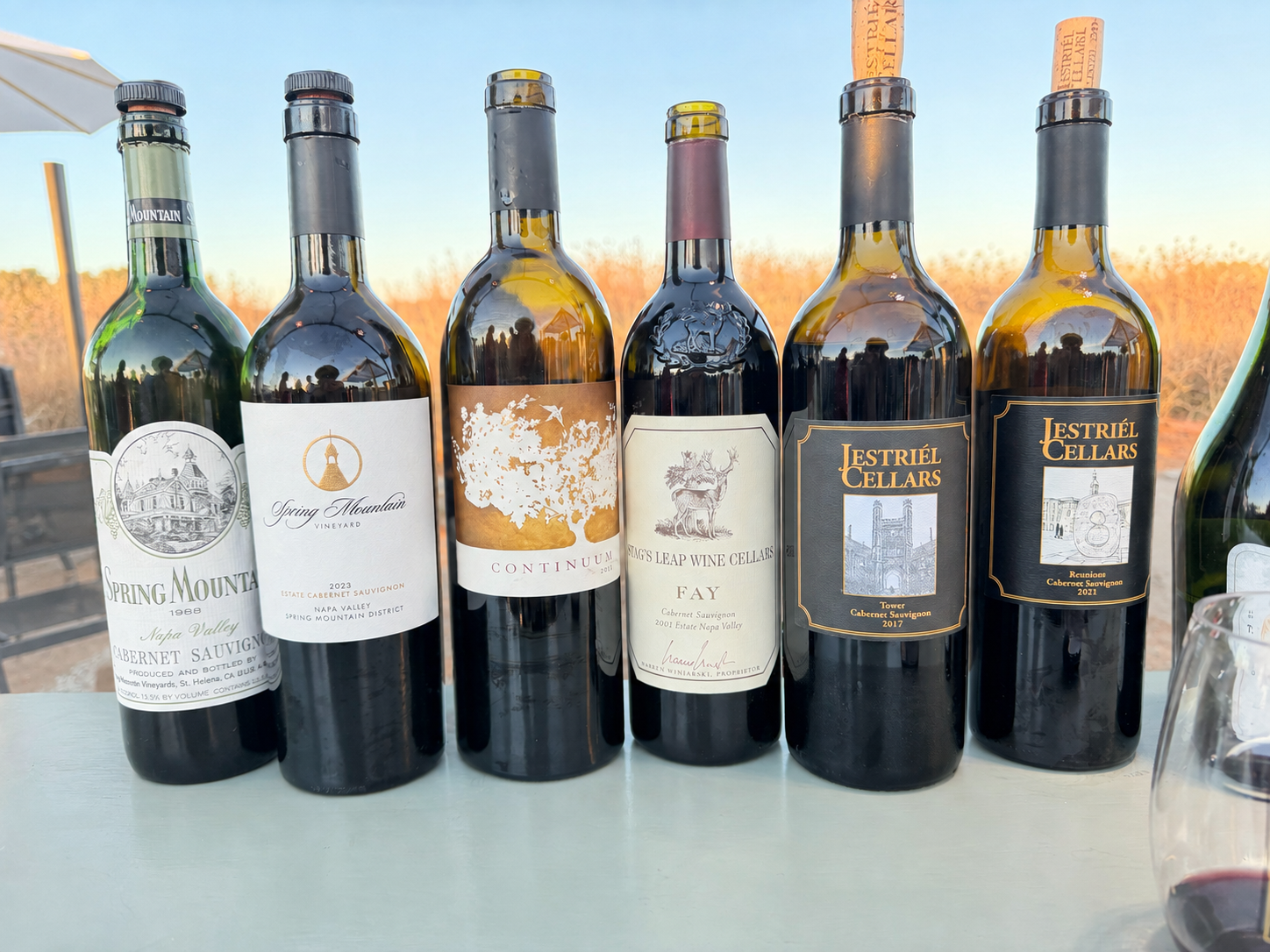 Six Napa Valley Cabernets at sunset: Spring Mountain 1988 and 2023, Continuum 2013, Stag's Leap Wine Cellars FAY 2001, and two Jestriel Cellars bottlings.