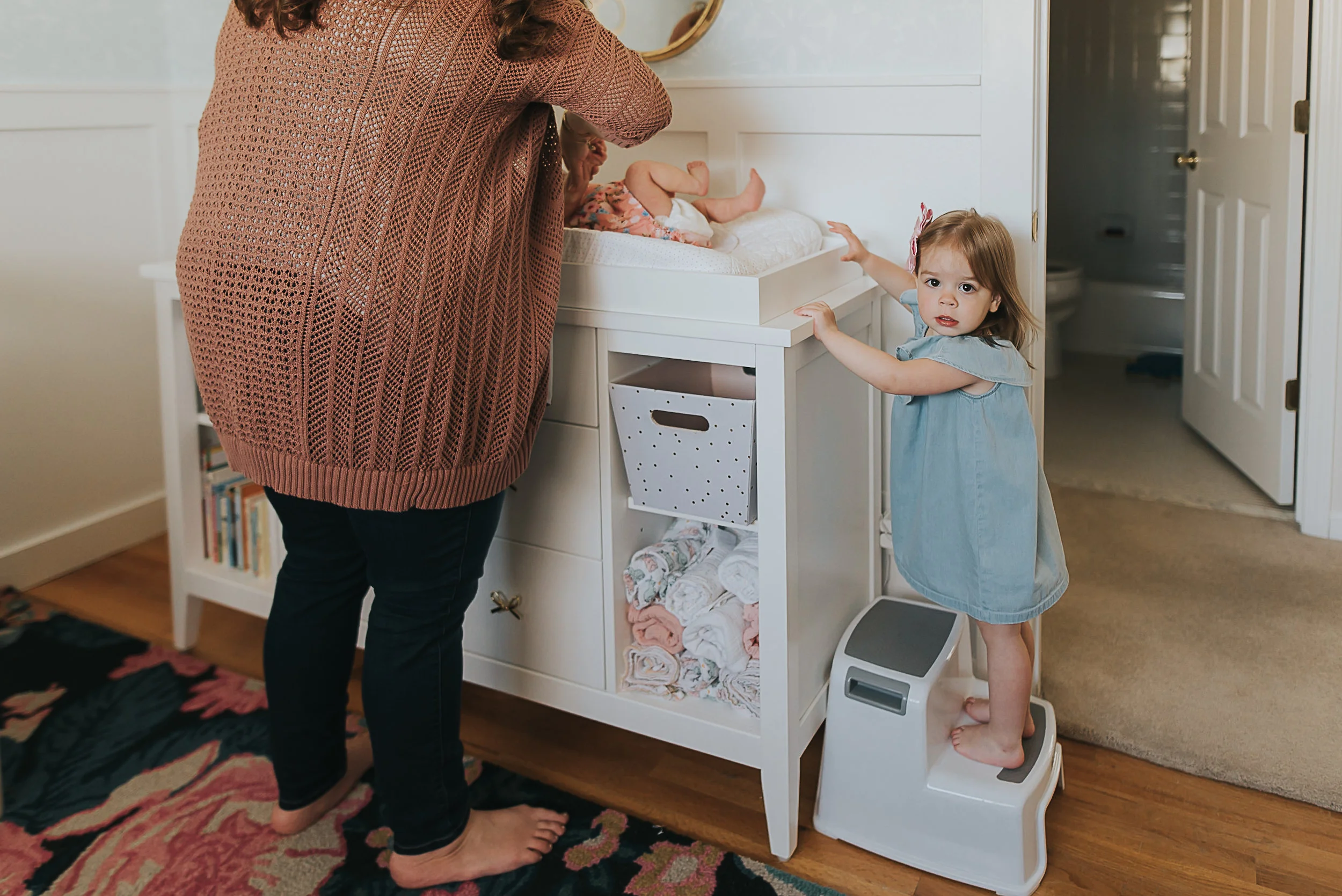 mom changing baby while sister looks on