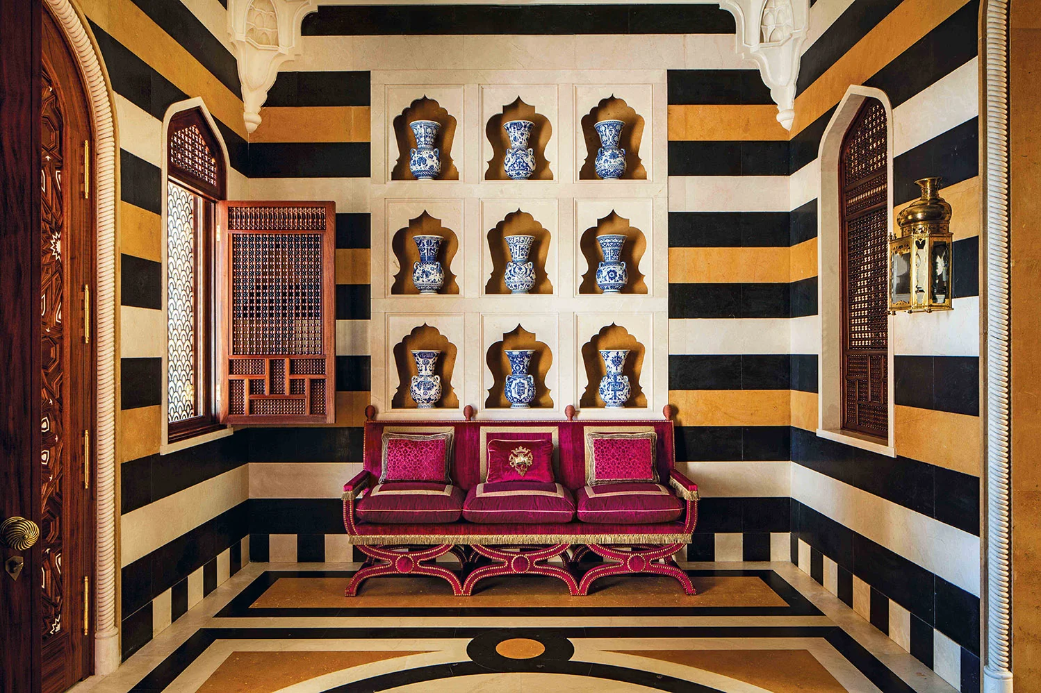 This is a wall of carved mrble alcoves, each of which contains a sixteenth century style Turkish blue and white mosque lamp. Mashrabiya grillwork adds a beautifully light touch to the space, as these shutters not only bring a certain prettiness, they also allow the space to be fllled with softly diffused daylight.
