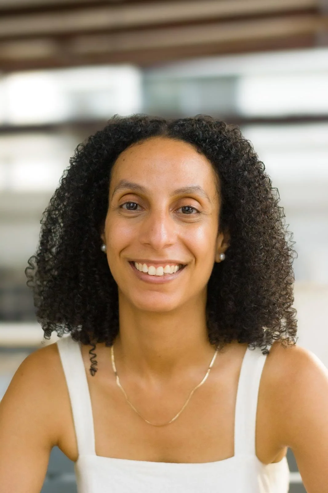 Woman with brown curly hair smiling in a cream-coloured tank top