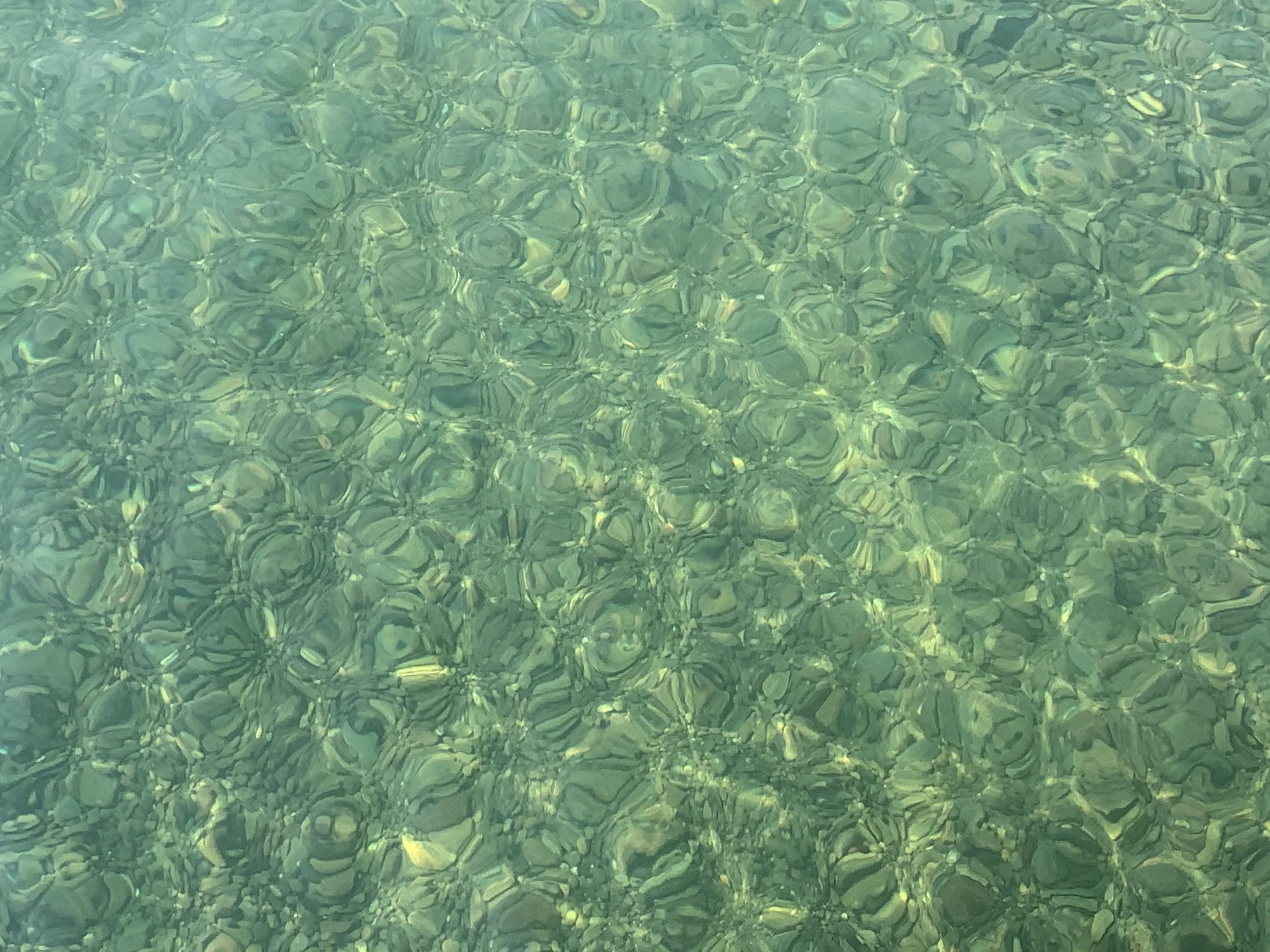 Clear green water with sunlight reflections and small rocks visible at the bottom.