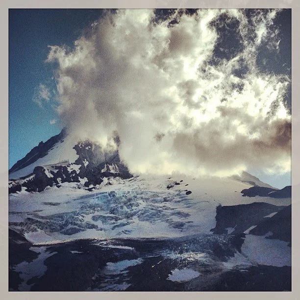 Snow-covered mountain with dark rocks and clouds in the sky.