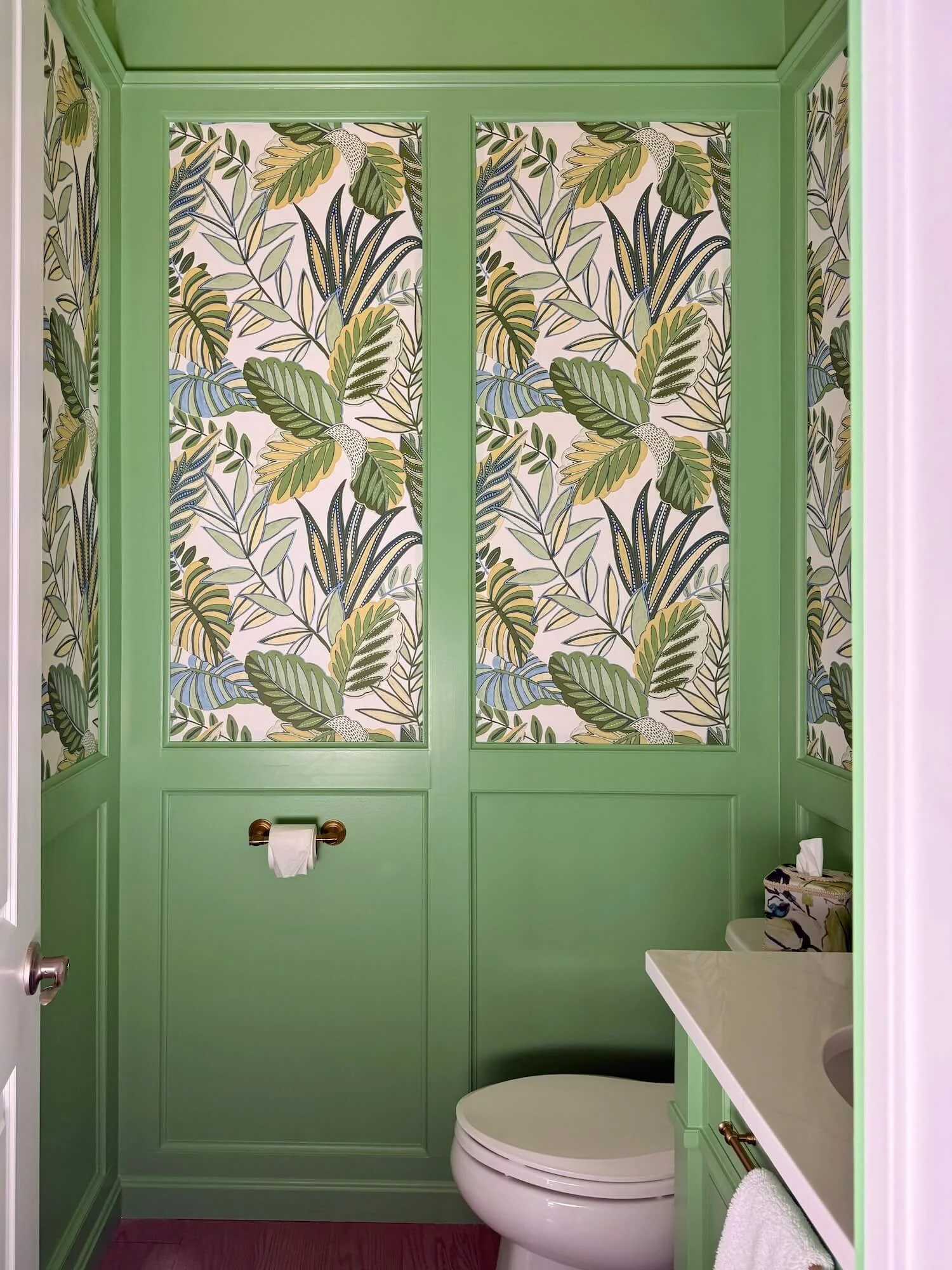 vibrant tropical leaf wallpaper in panels of a small powder room