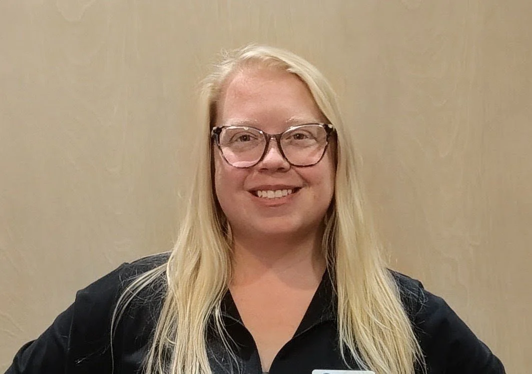 A woman with blonde hair, glasses, and a black shirt smiling at the camera.