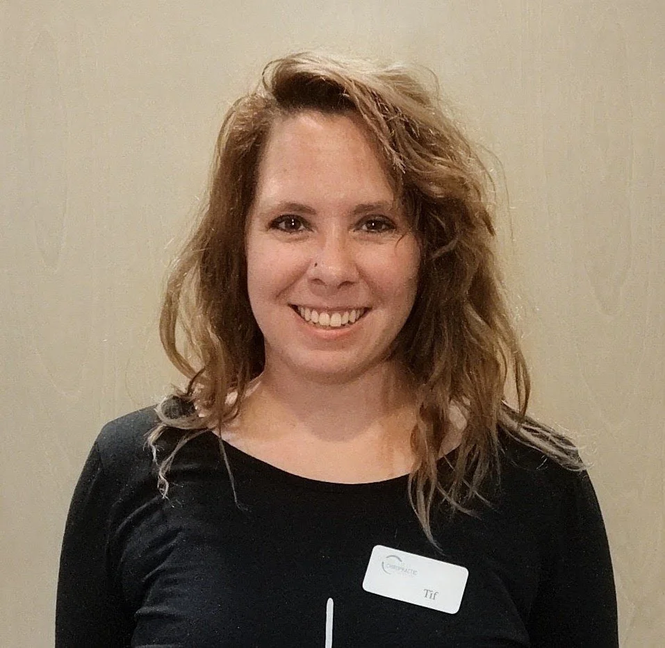 Woman with wavy, shoulder-length brown hair, smiling, wearing a black top and a name badge that reads "Tif".