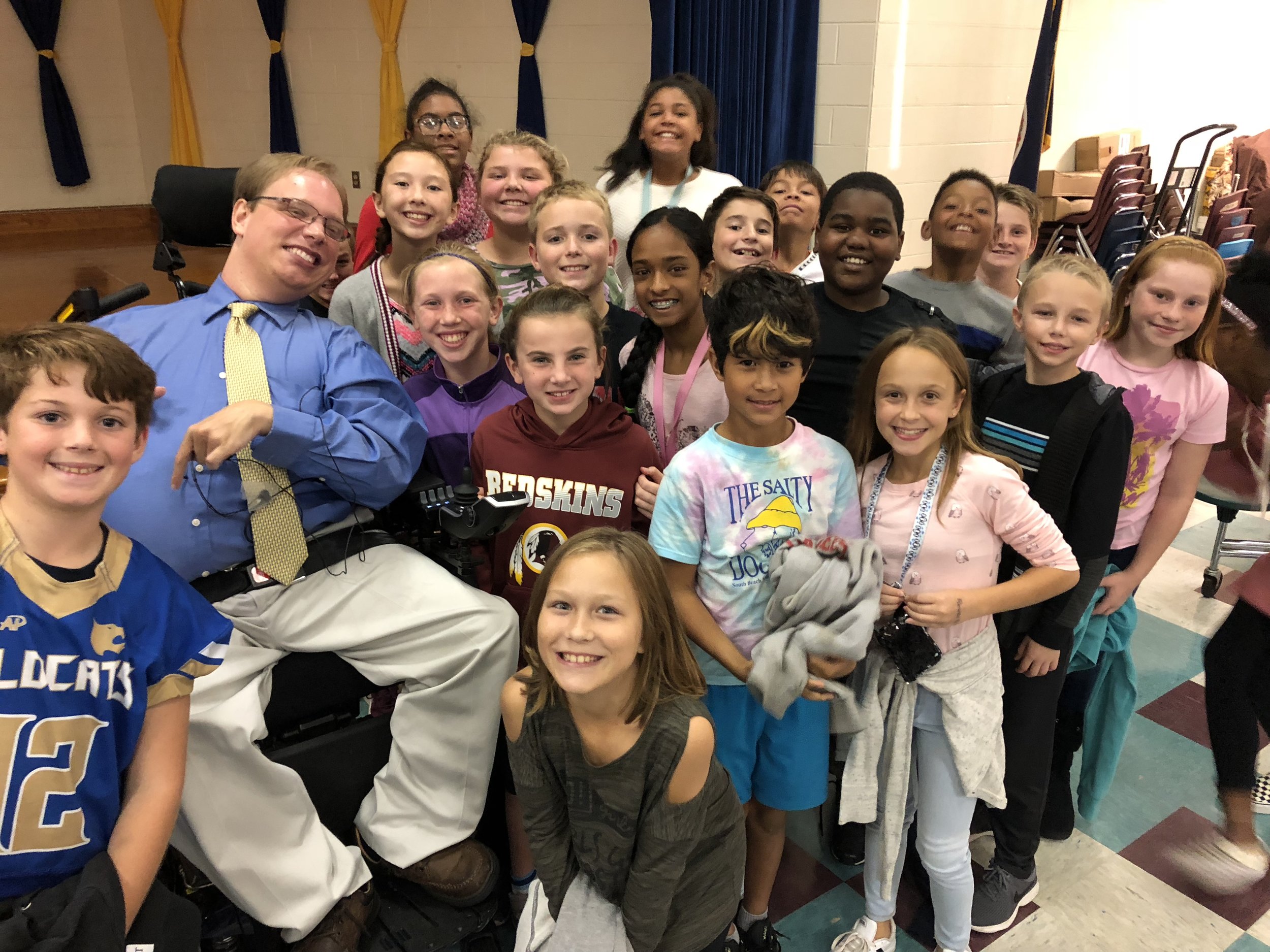 PHOTO: Matthew taking a group photo with several smiling fourth and fifth graders from Woolridge Elementary School after his Positively Inclusive presentation.