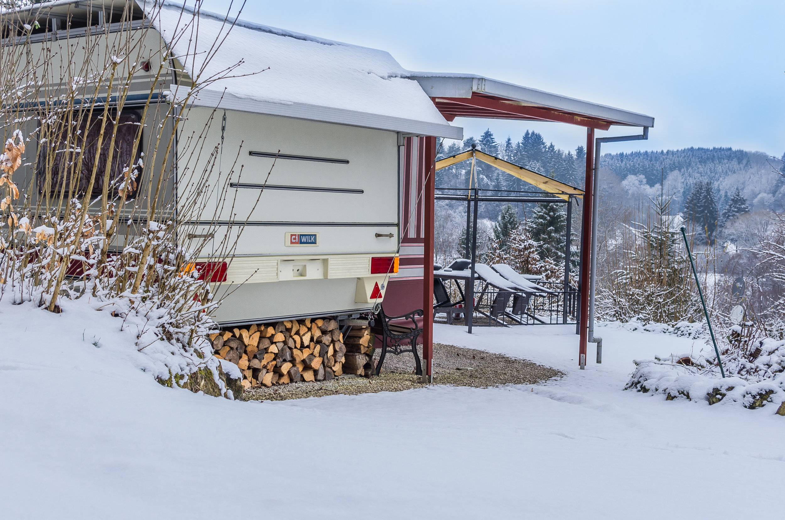 Wohnwagen umgeben von Schnee, Holz unter dem Wohnwagen geschlichtet