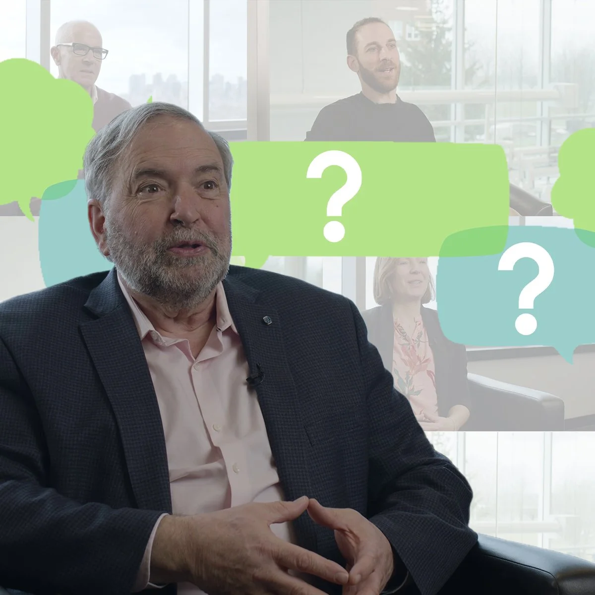 Un homme âgé avec une barbe grise en costume parlant lors d'une interview dans une salle de réunion moderne avec plusieurs personnes en arrière-plan. Il offre uue formation en vidéo tournée au studio de tournage.