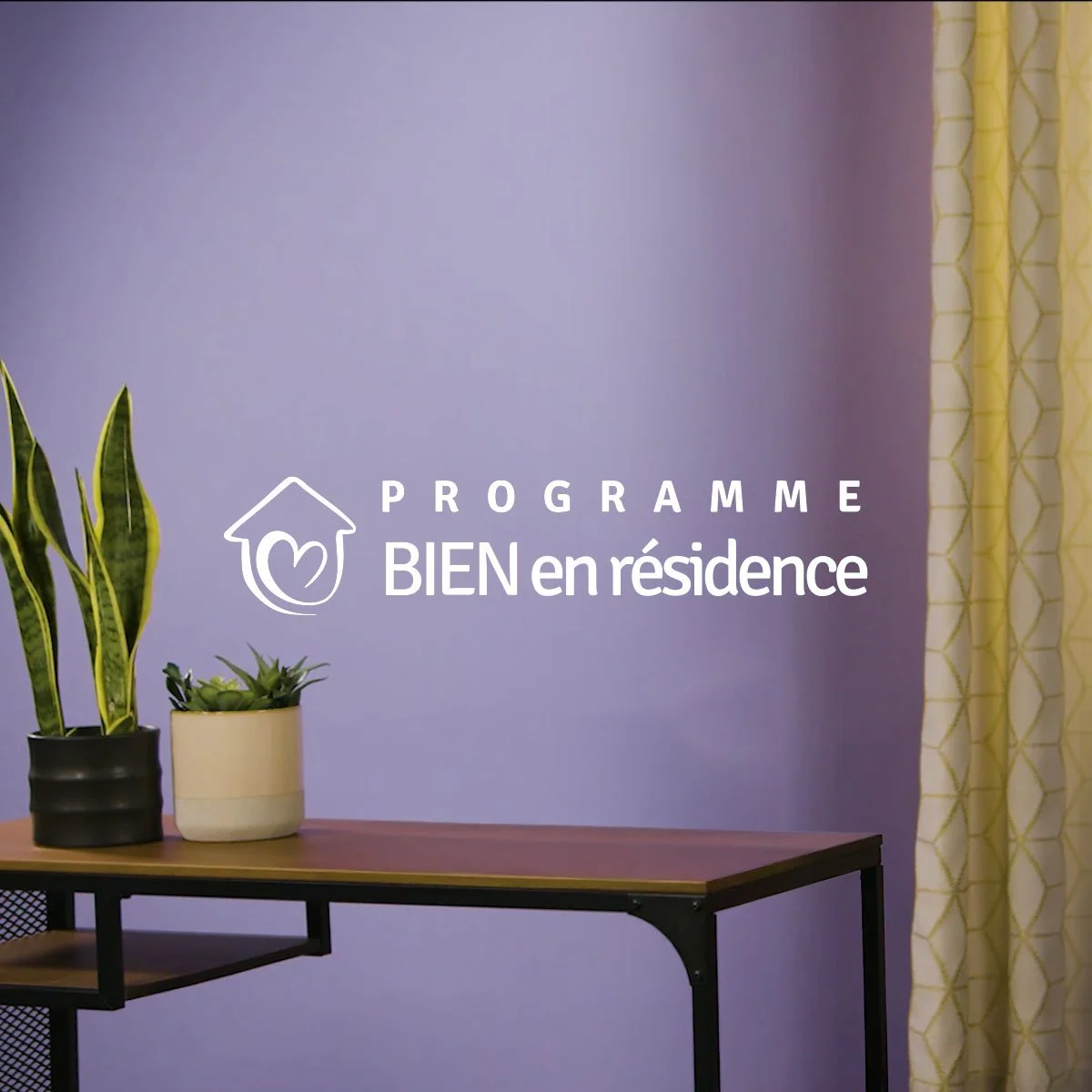 Logo et texte du programme Bien en résidence affichés sur un mur violet à côté d'une table avec des plantes vertes en pot. Cette vidéo présente l'organisme a but non lucratif et ses bienfaits en Estrie.