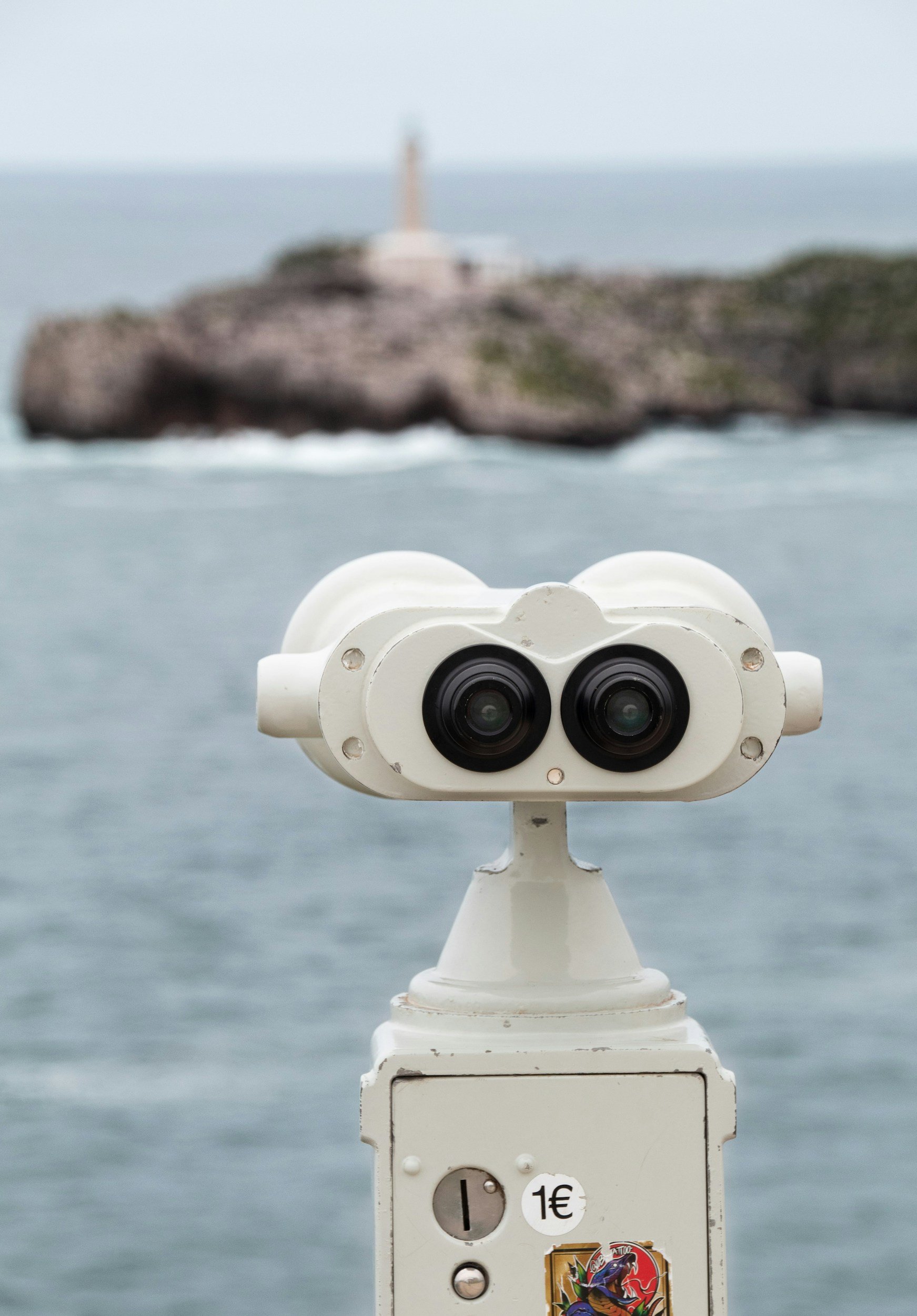 fixed public binoculars with a blurred lighthouse in the distance
