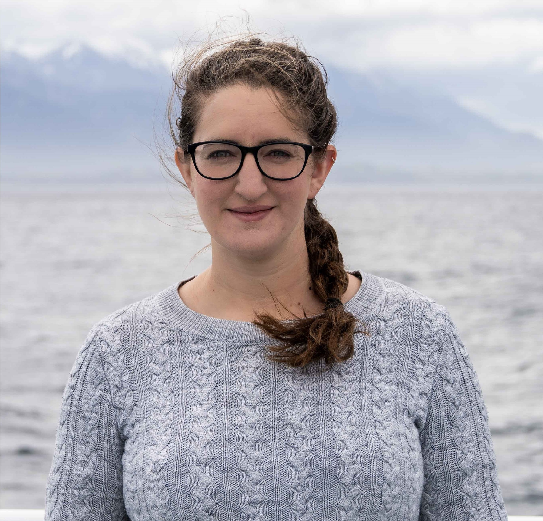 Rachel Hale stands in front of the ocean with some mountains blurred in the distance