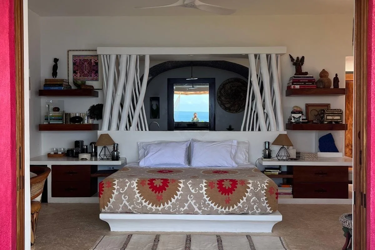 Sun suite at Casa Papelillo framed by a fuchsia doorway, with a branch headboard screen and ocean view, interiors by Amathea