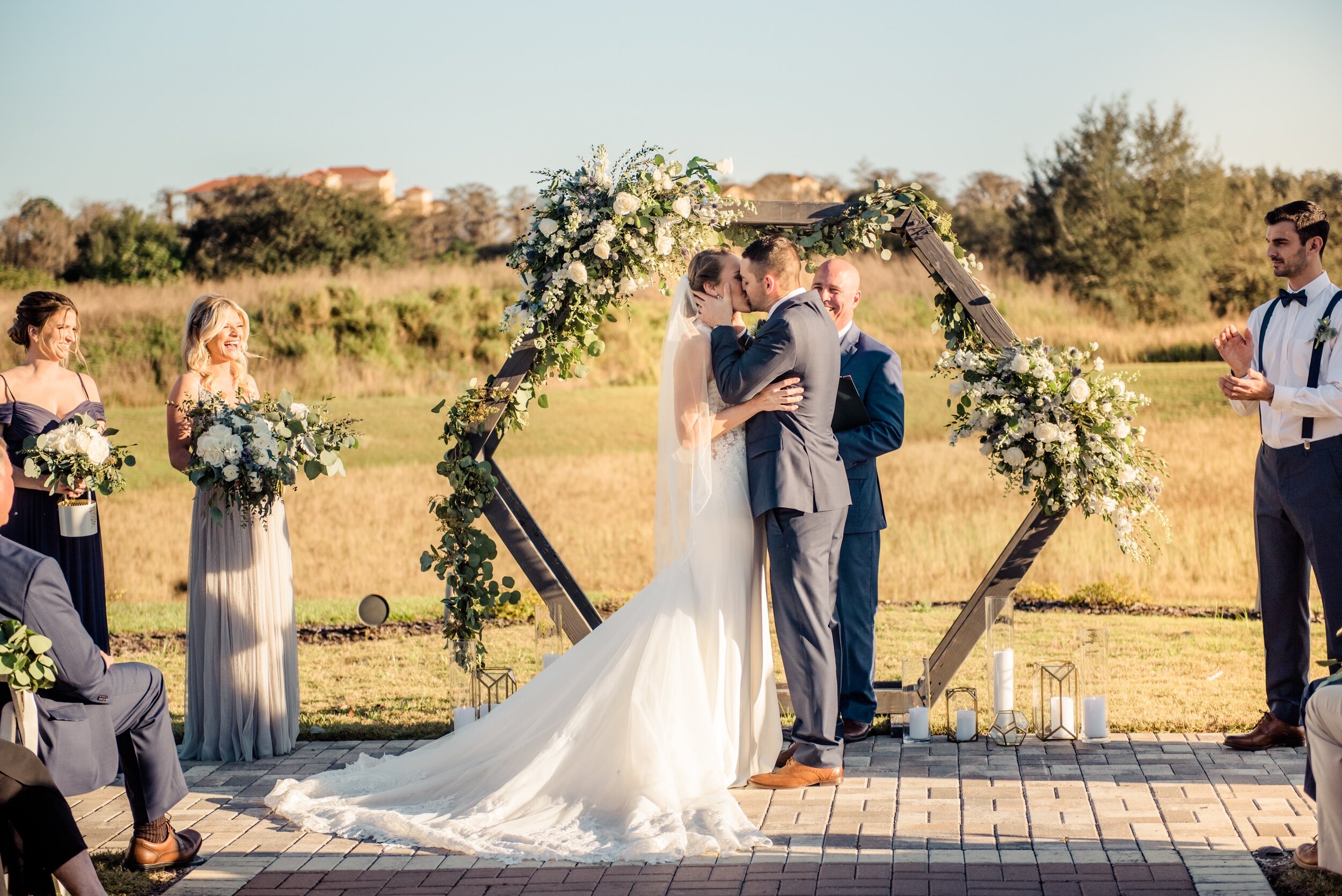 The bride and groom in front of the hexagon wooden arch at Formosa with white and green floral and geometric vases. Sealed with a kiss!!