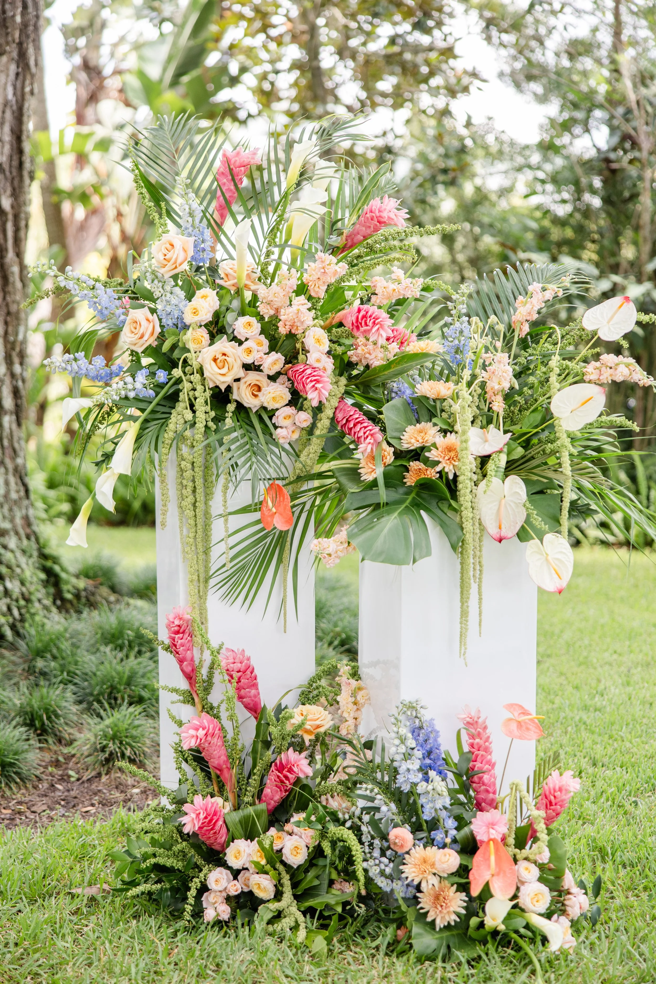 Soft tropical floral installation featuring pastel blooms and ground arrangements for an elevated event, designed by Bluegrass Chic, an Orlando event florist.