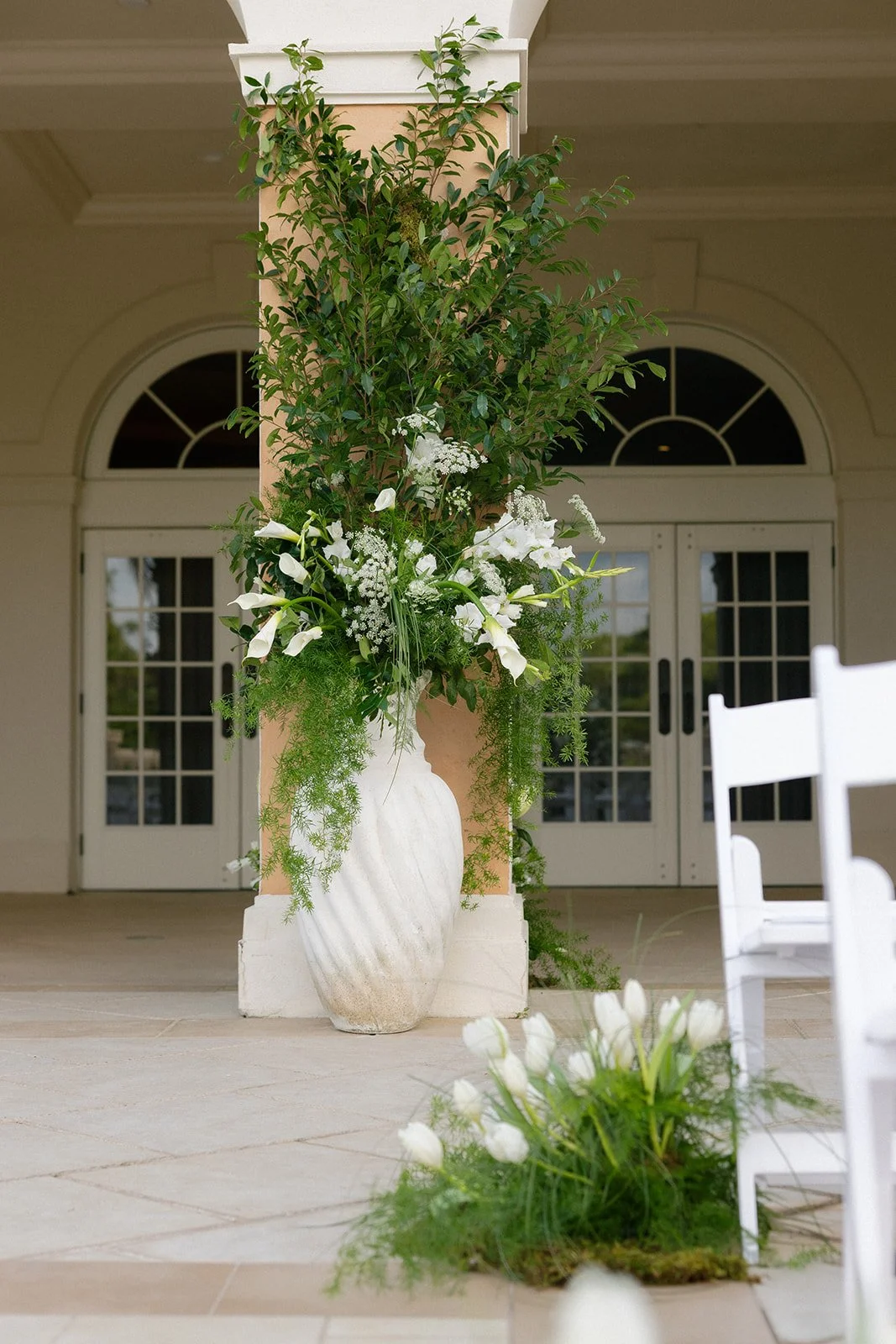 Statement urn arrangements filled with white flowers and greenery framing the Crane Club wedding patio entrance, designed by Bluegrass Chic.