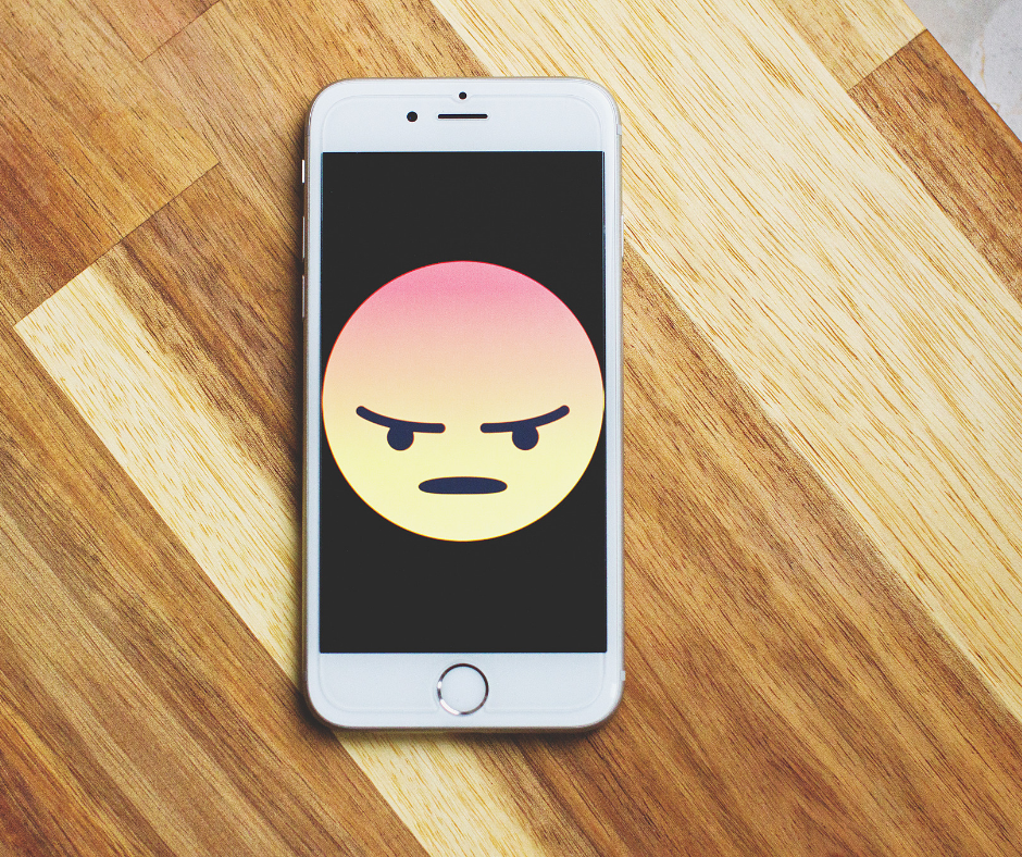 An angry face emoji on black background on smartphone on a wooden desk