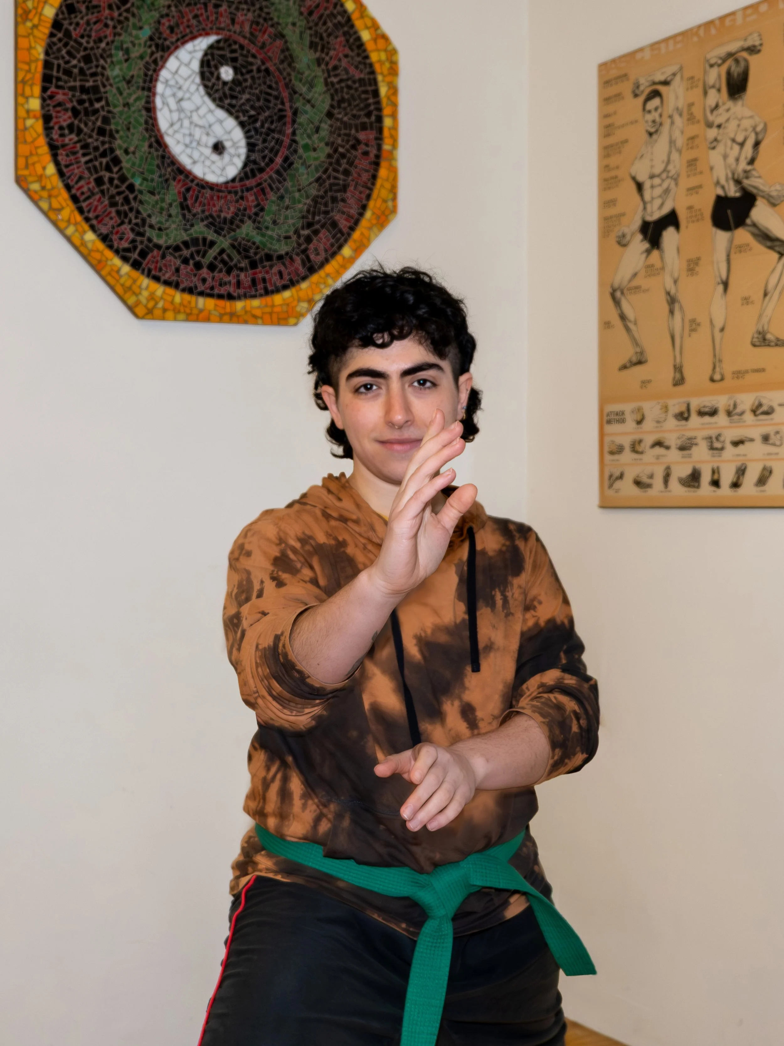 A person with dark wavy hair in a martial arts stance looking at the camera