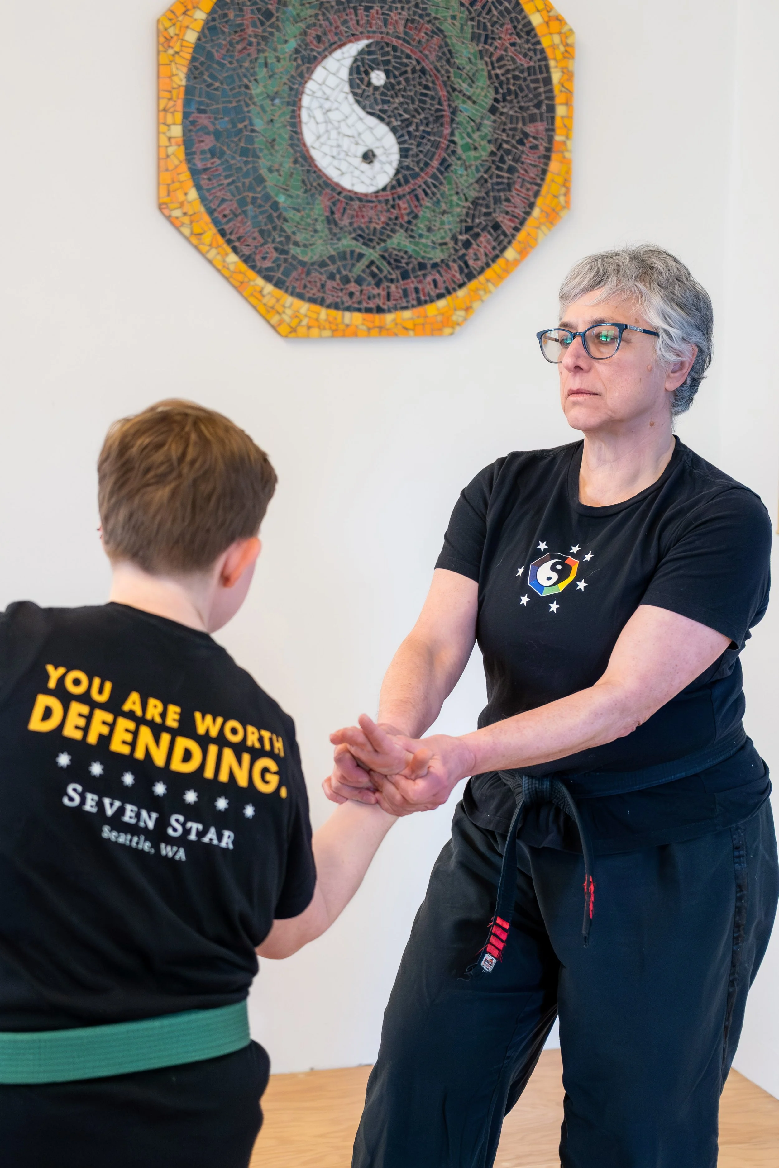 A woman with grey hair and glasses is putting a person in a joint lock