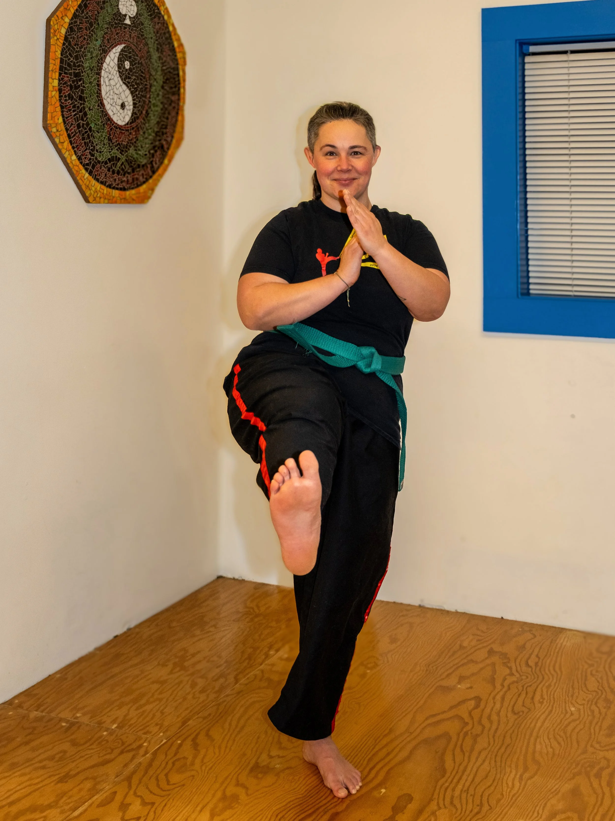 A person with hair in a ponytail on one leg kicking towards the camera