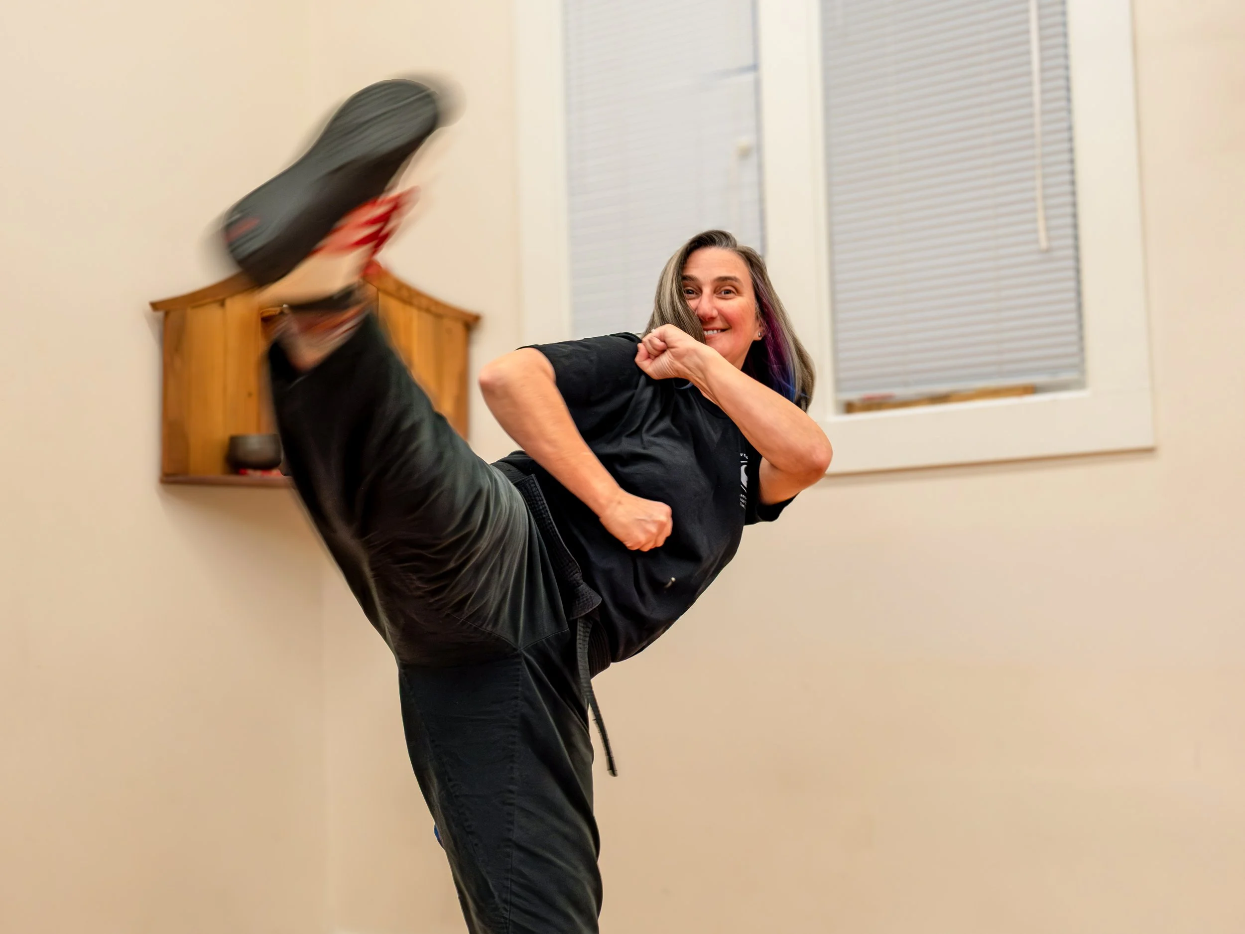 A woman with long grey hair is kicking towards the camera