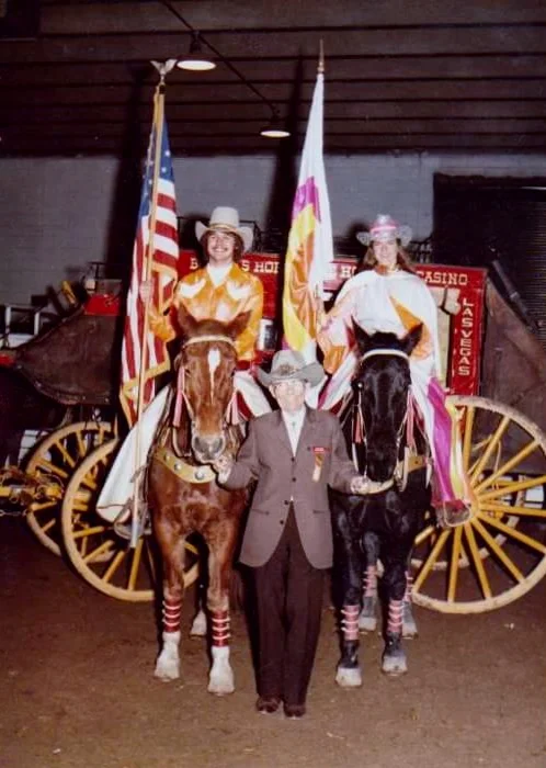 The 1982 Varsity Red Team Majors, Gary Feazell and Patty Miller, pose with Westernaires Founder and Director, Elmer E. Wyland, in the paddock of National Western Stock Show