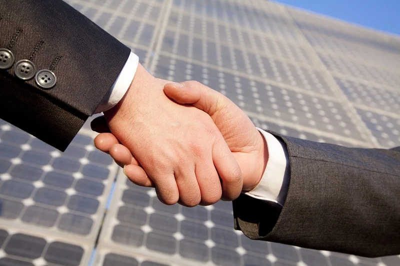 Shaking hands in front of solar panels