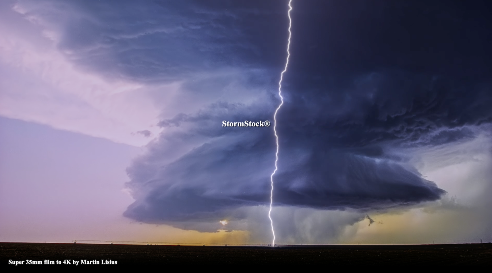 Massive, rotating blue supercell thunderstorm with bolt of lightning at dusk, Texas