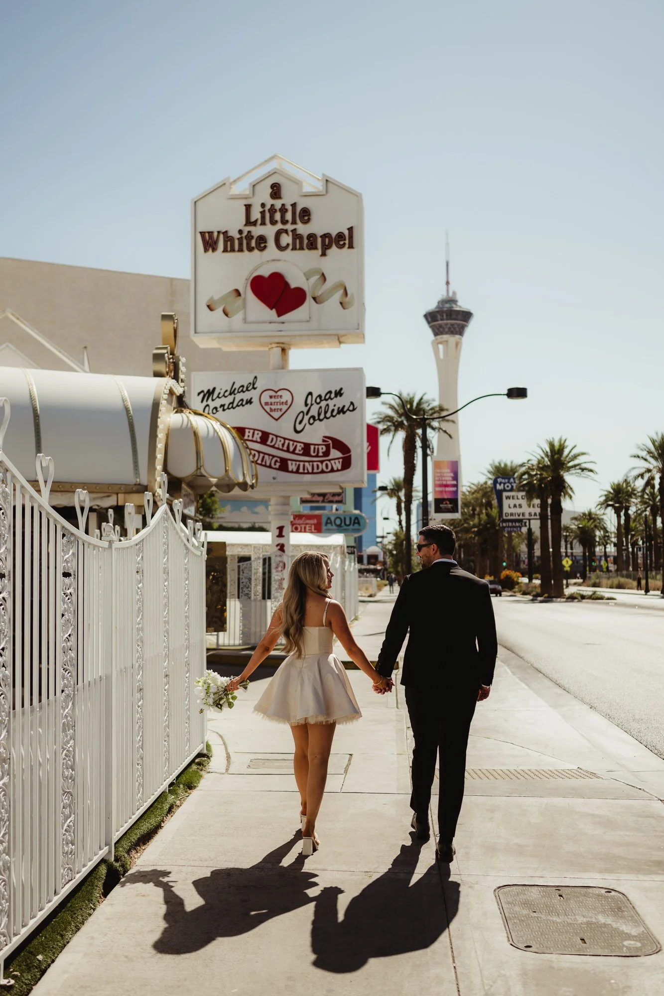 An elopement couple walks toward the famous Little White Chapel sign