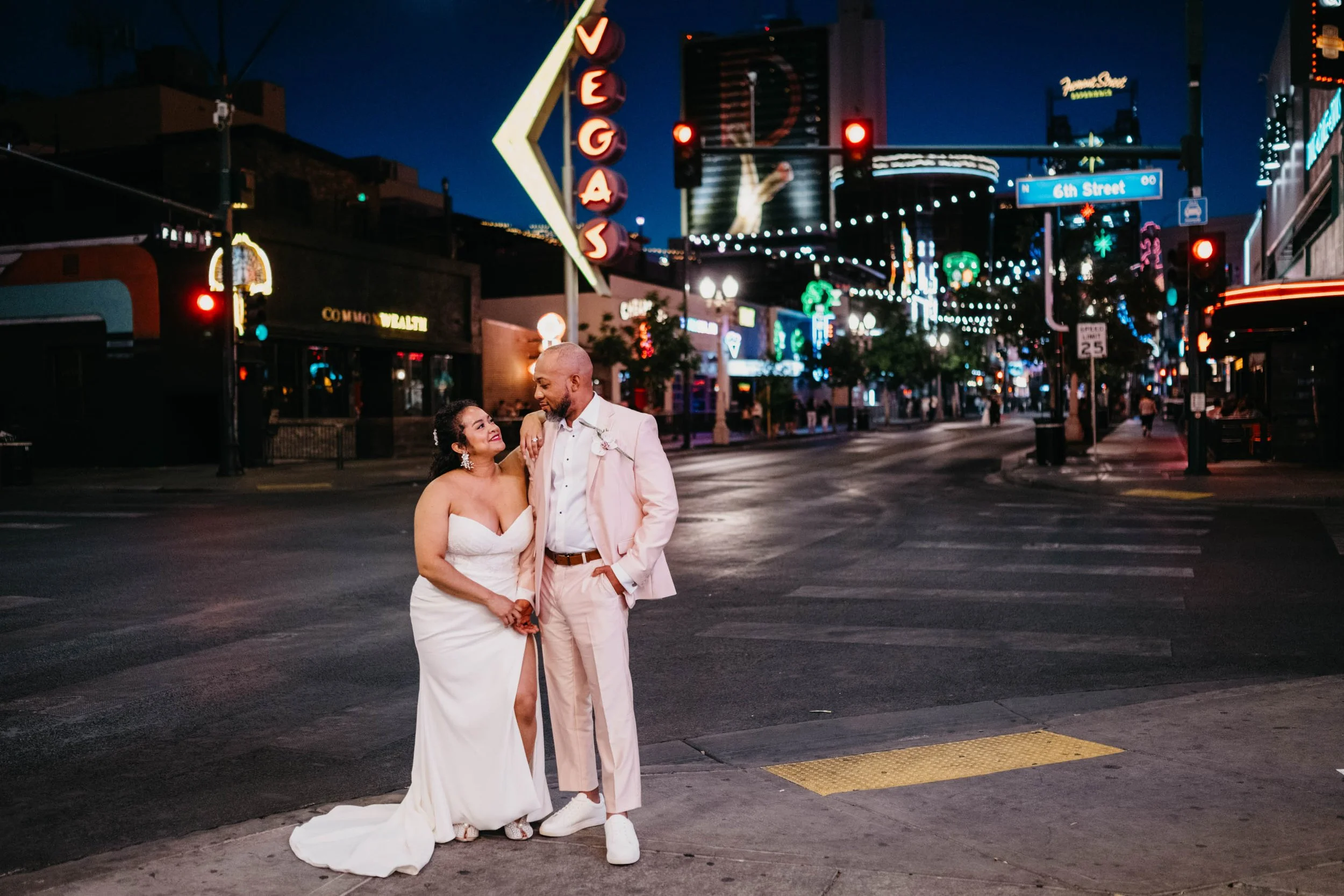 A Black couple in wedding attire poses together on Fremont Street in front of neon lights