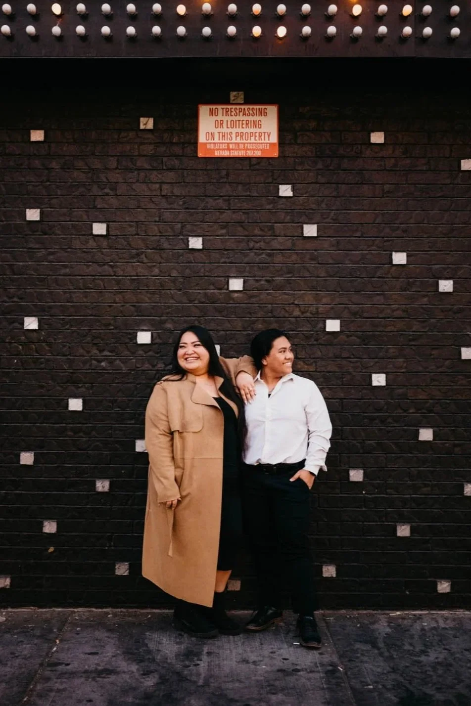 two engaged women pose for a photo on fremont street in front of a black wall with white checkers