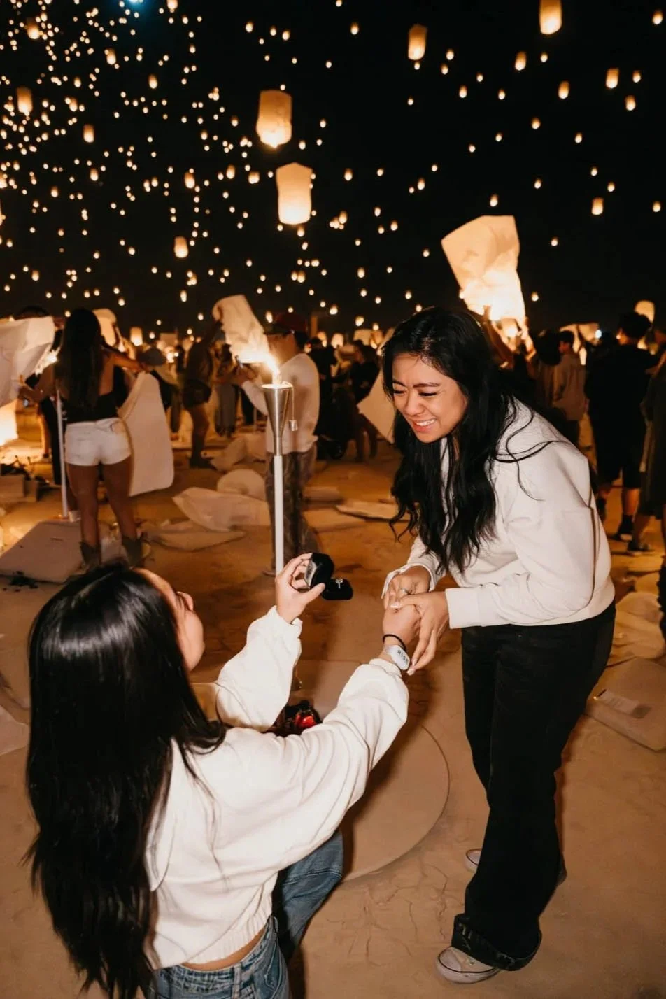 a woman in a white sweater proposes to another woman in a white sweater at the RISE festival with lanterns in the air behind them