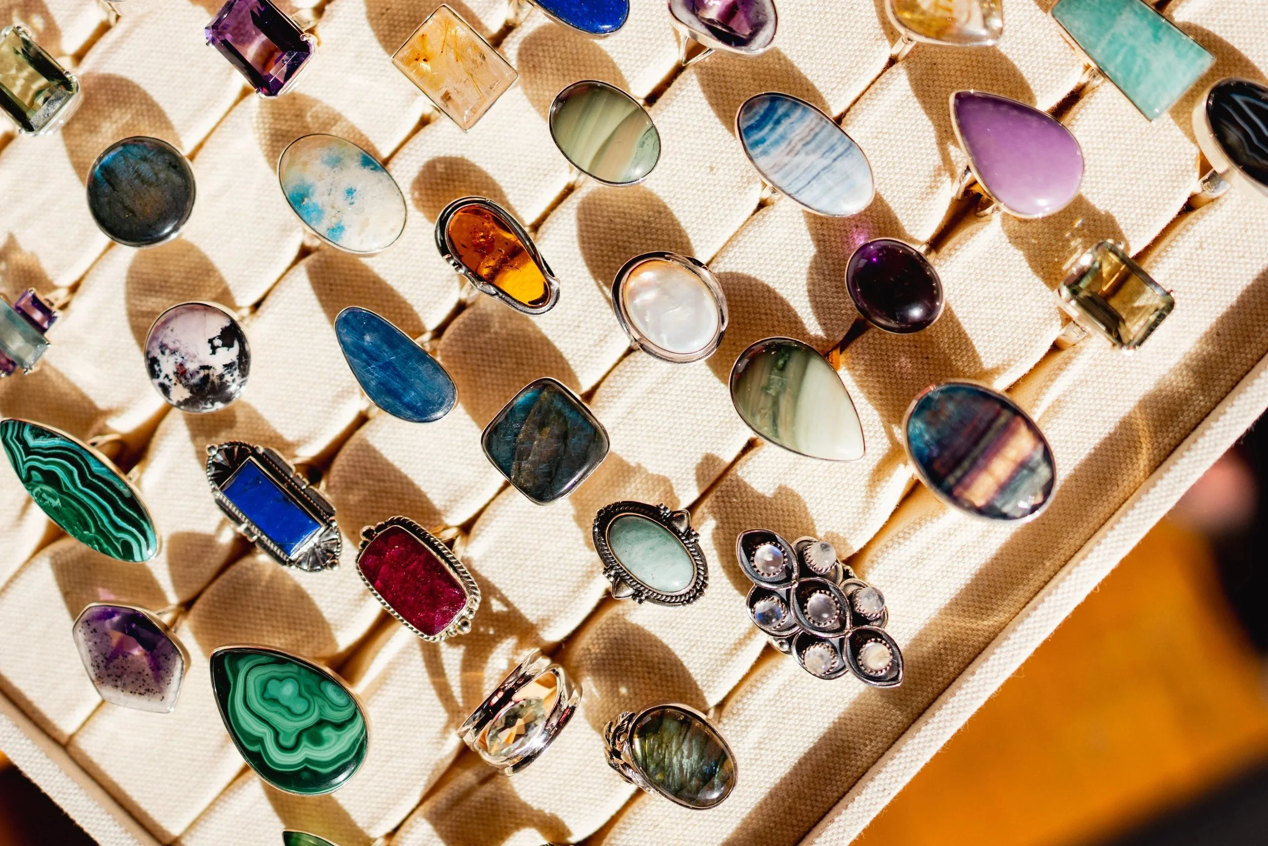 Various colorful gemstone rings displayed on a beige jewelry stand in a jewelry shop.