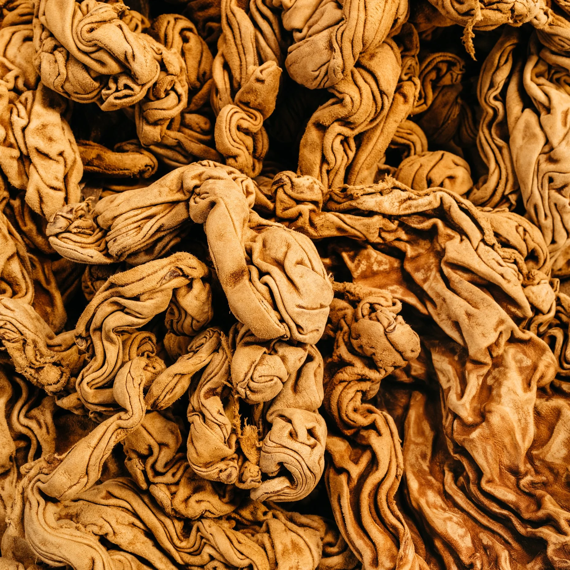A pile of tangled, wrinkled, beige leather.