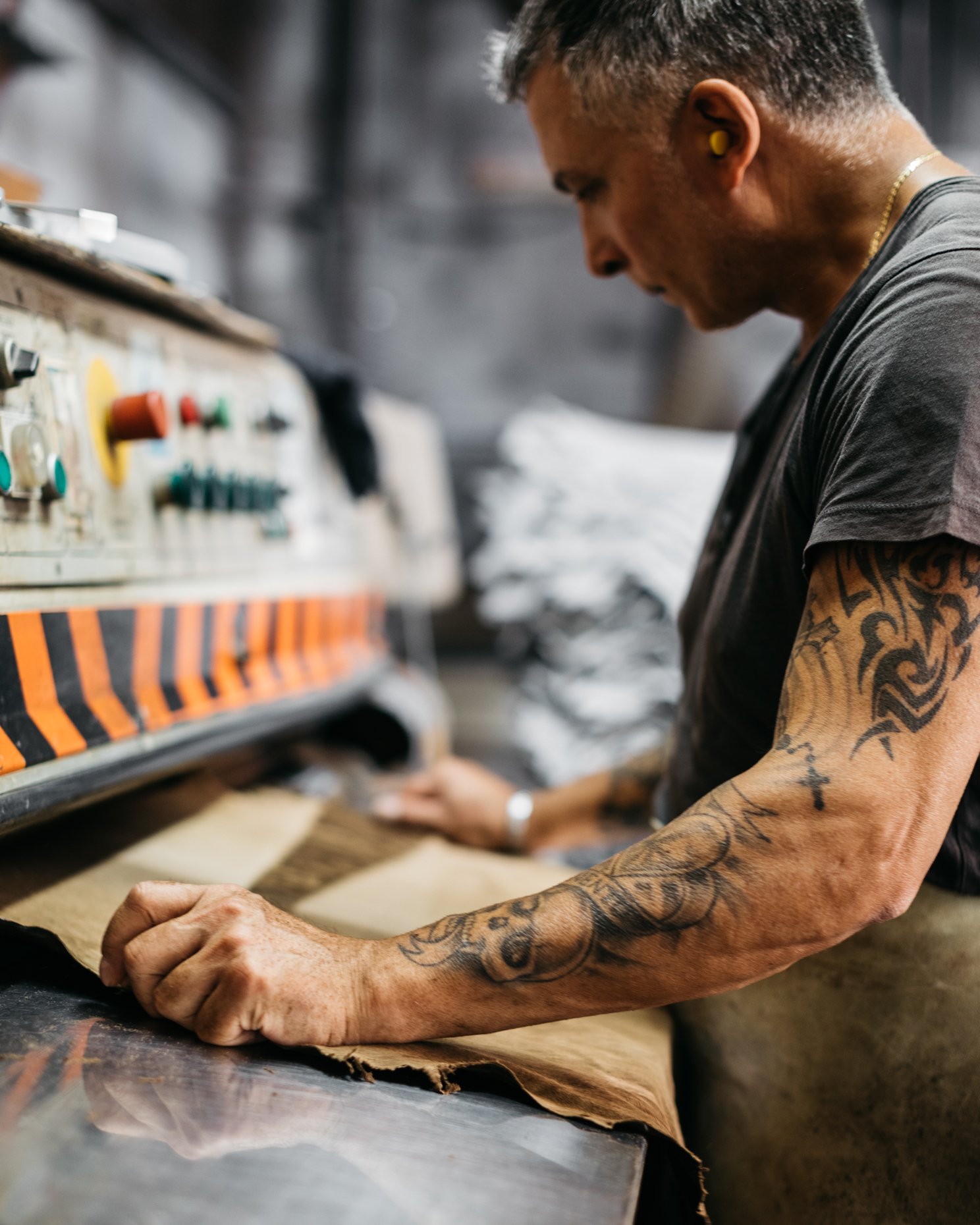 A tattooed man working with leather using a machine in a workshop