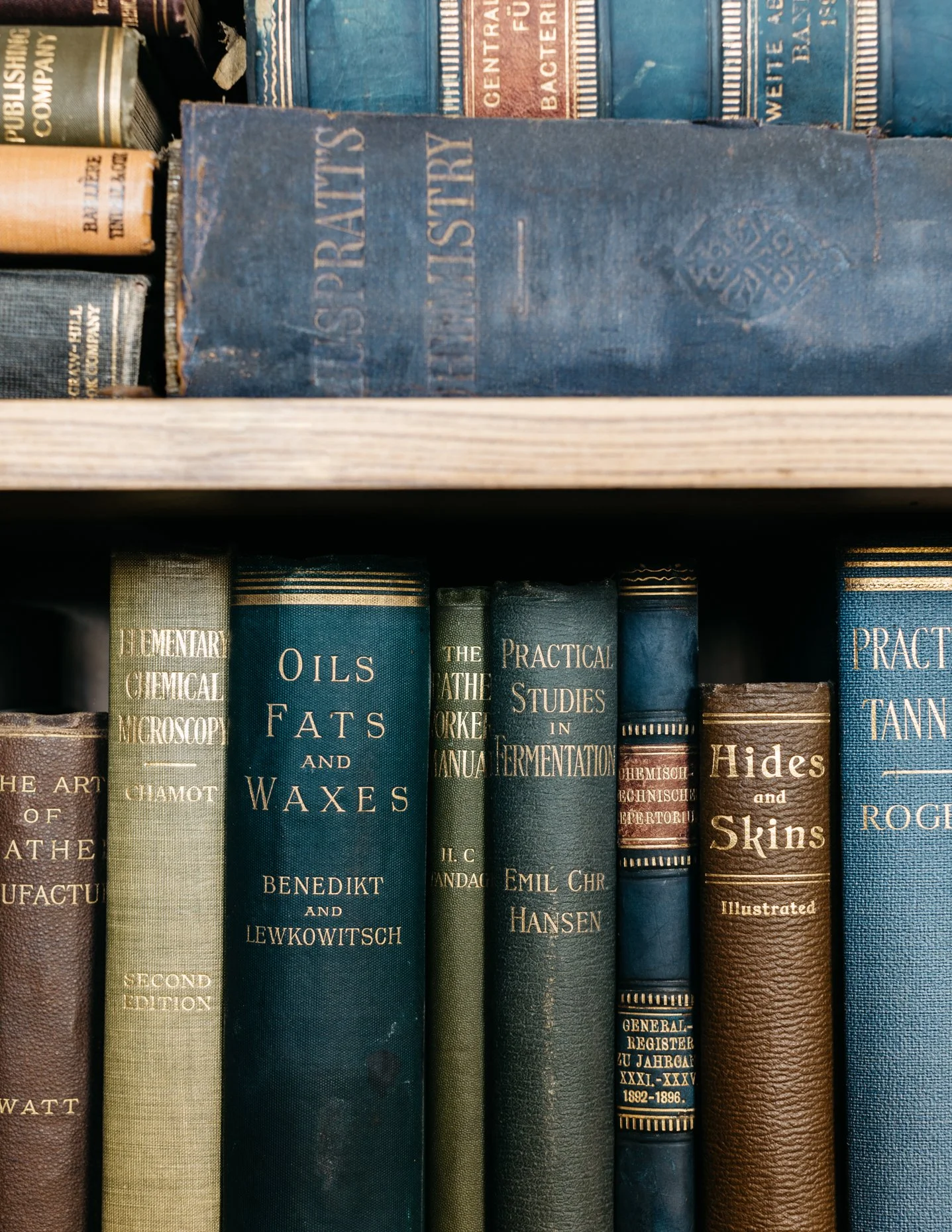 Close-up of vintage books on a shelf, including one titled 'Oils Fats and Waxes' and another 'Hides and Skins'.