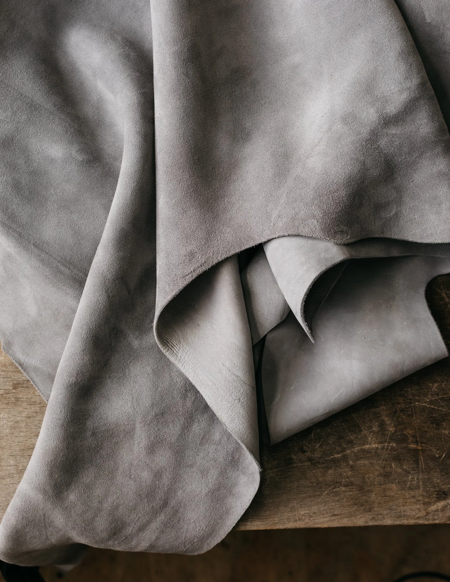 Close-up of gray leather and suede fabric draped over a wooden surface.