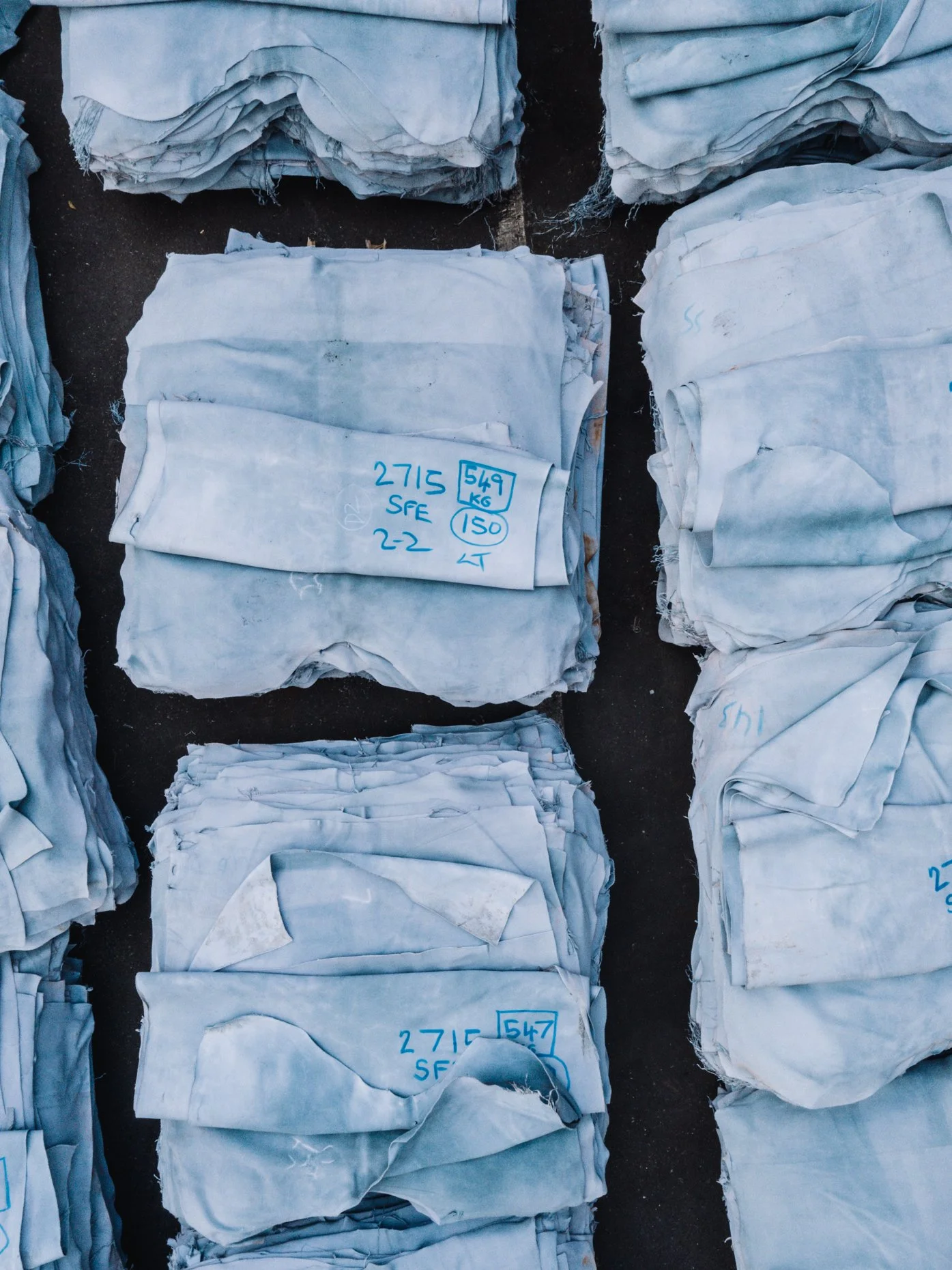 Multiple stacks of leather hide "blues" and organized, with handwritten labels in blue ink indicating sizes and weights.