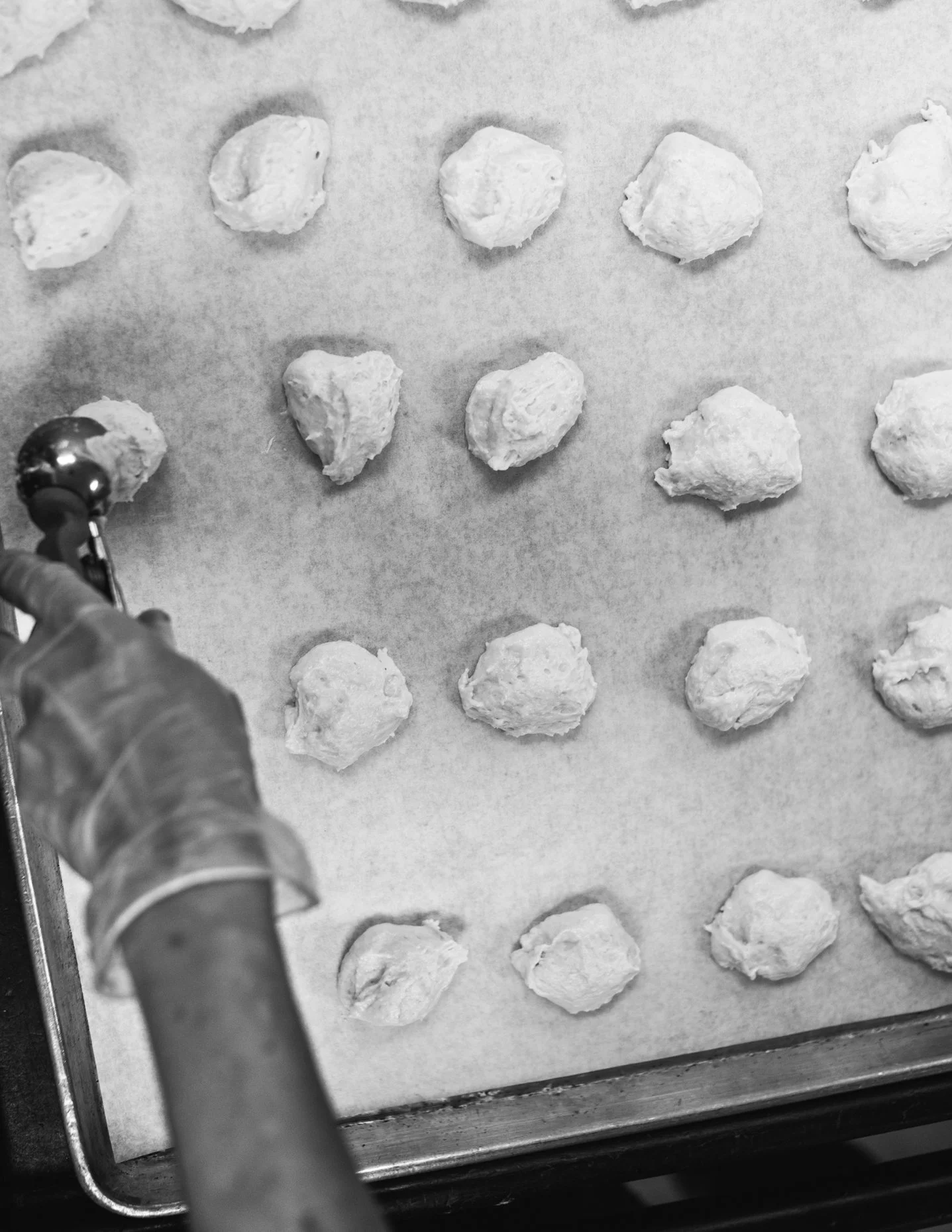 A person wearing gloves using a cookie scoop to portion out dough onto a baking sheet lined with parchment paper.