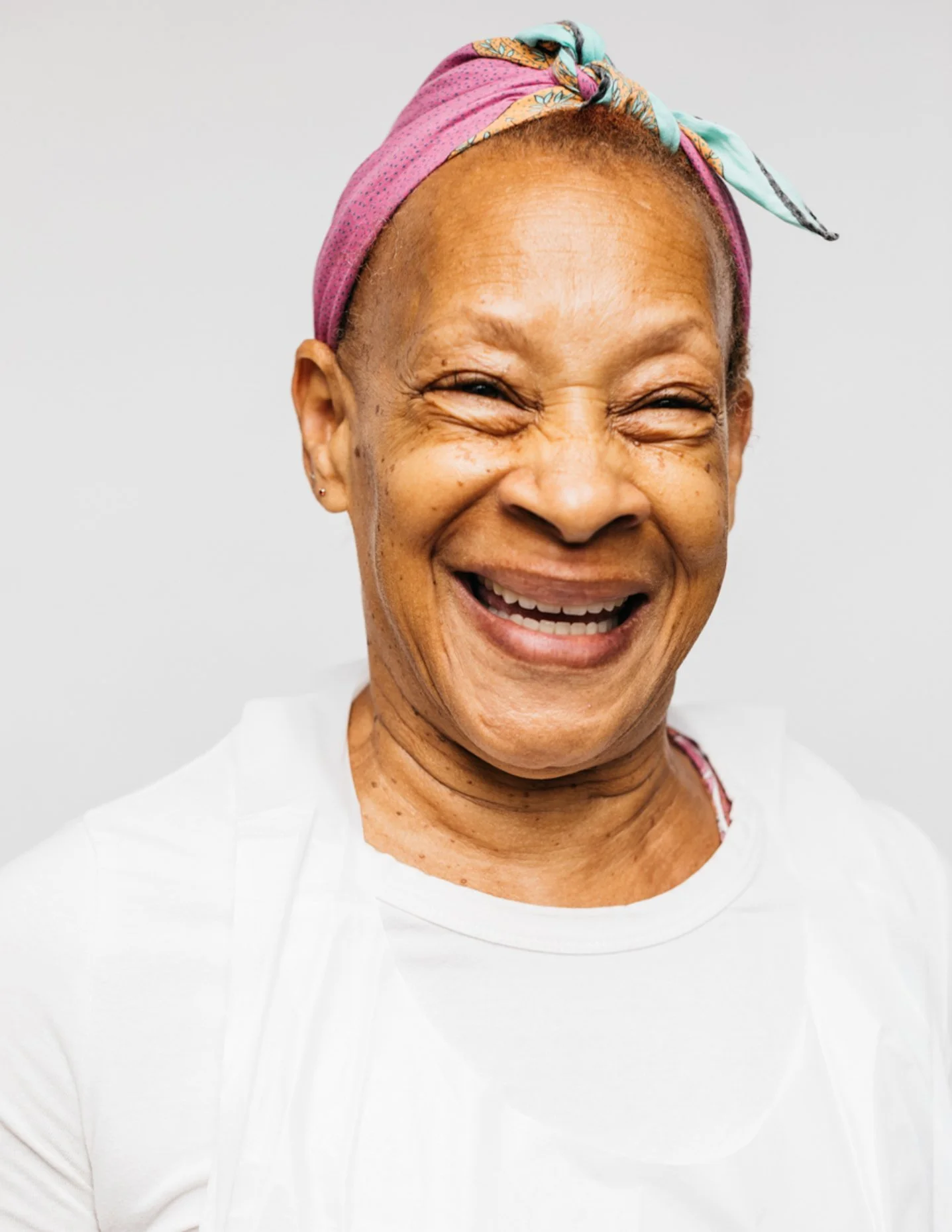 Smiling woman with a colorful headscarf and white shirt.