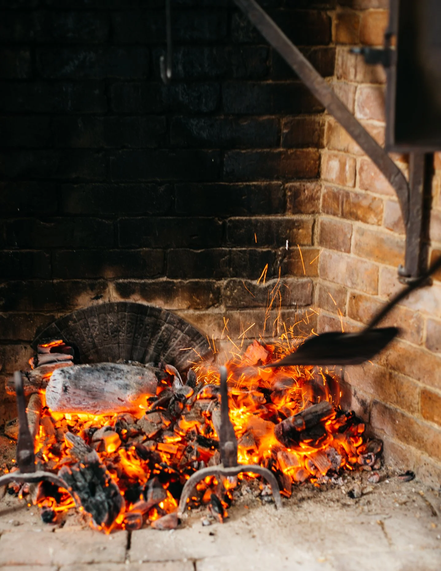 A fireplace with glowing embers and bright orange and yellow flames, set against a brick wall background.