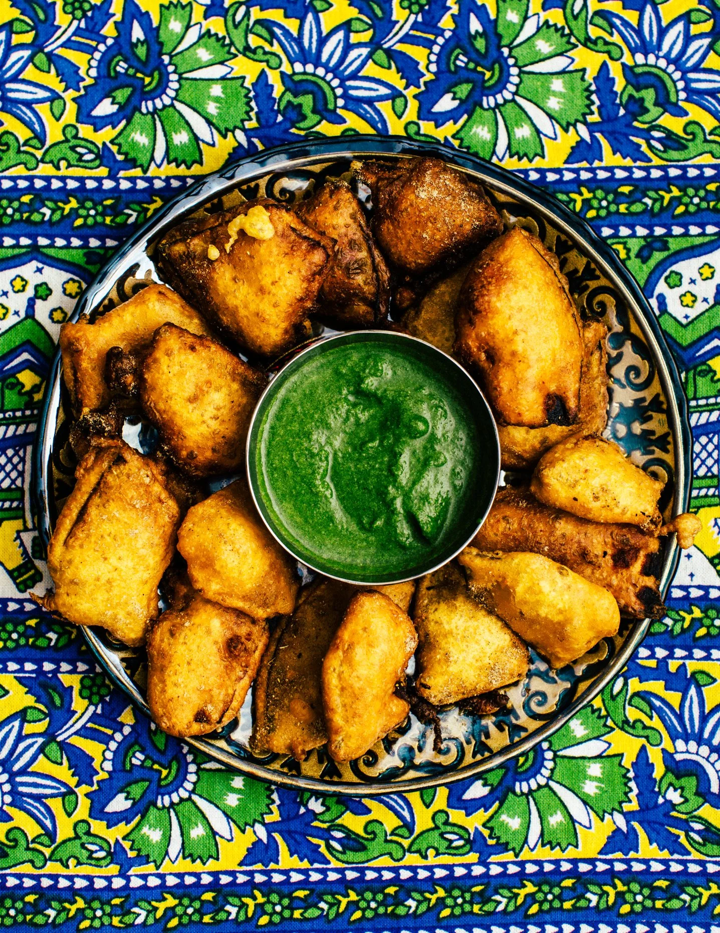 Plate of fried snacks with green dipping sauce on a colorful patterned cloth.