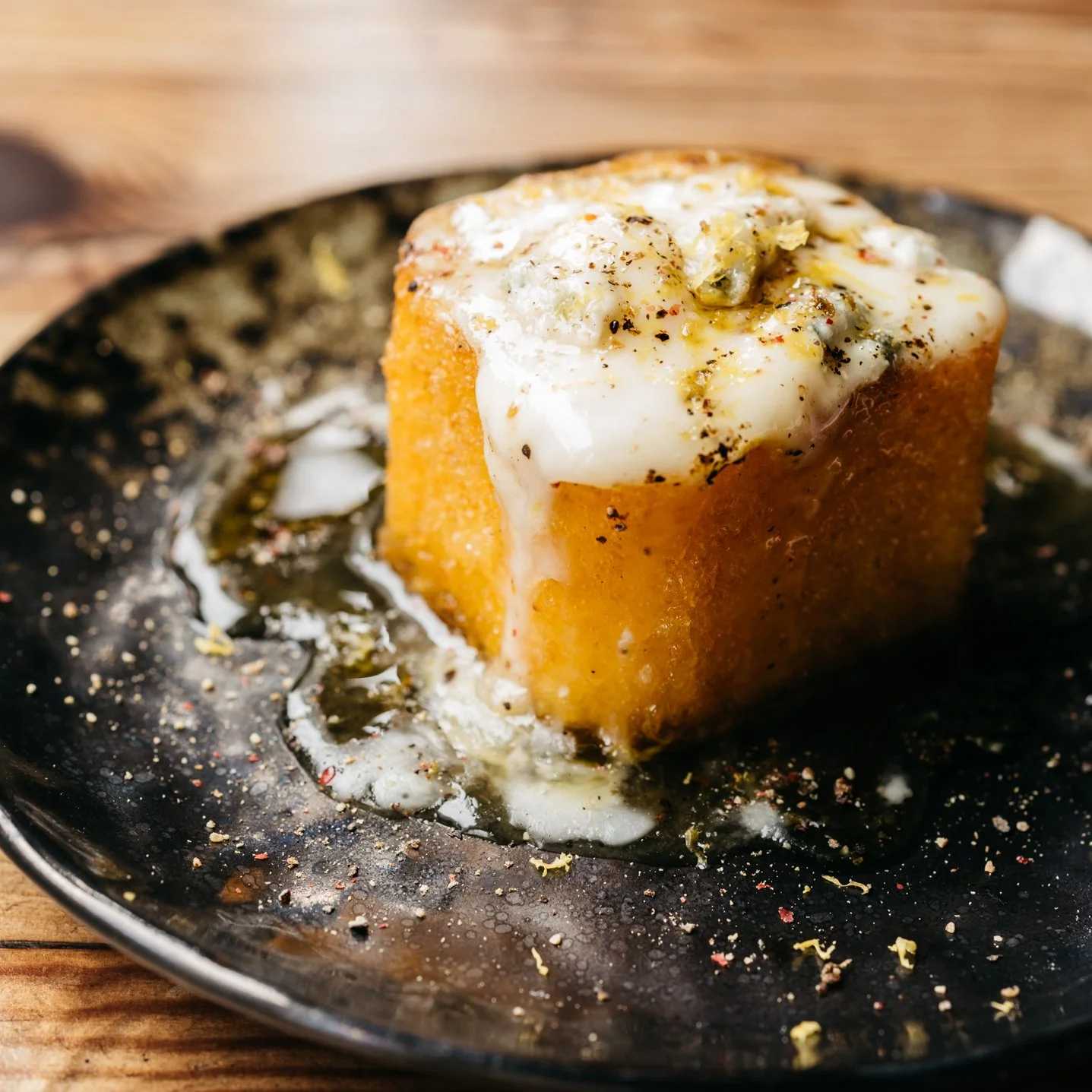 A serving of polenta topped with melted cheese, herbs, and black pepper on a dark plate.