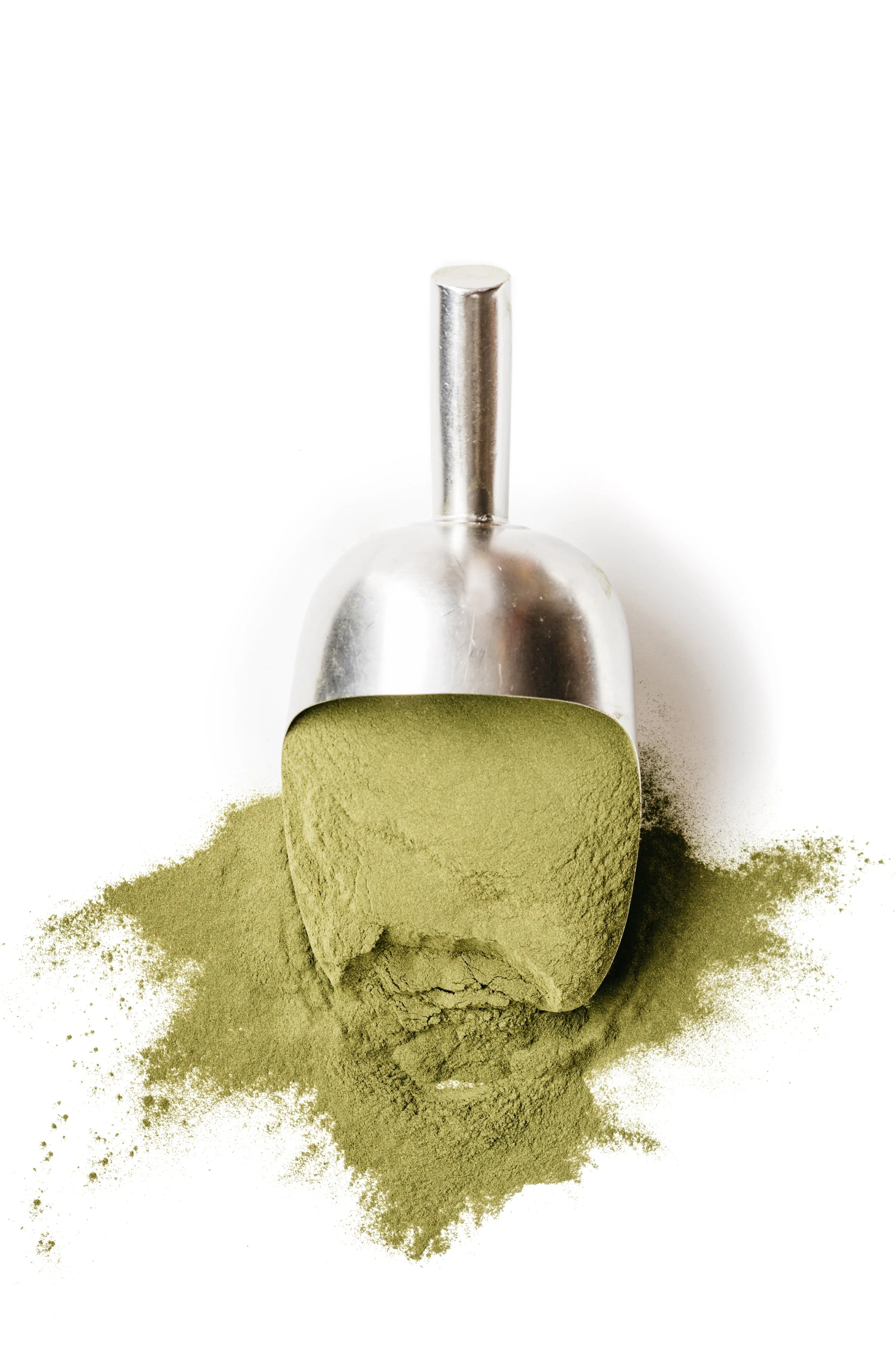 Metal scoop filled with vegetable powder placed on white surface.