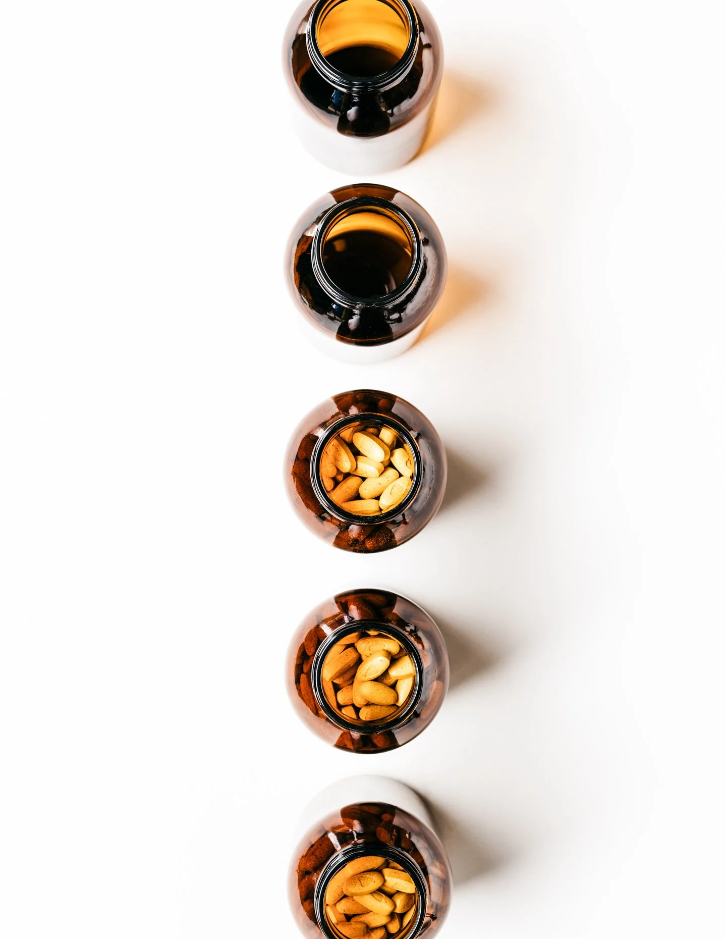 Top view of five brown medicine bottles arranged vertically, with three containing pills inside on a white surface.